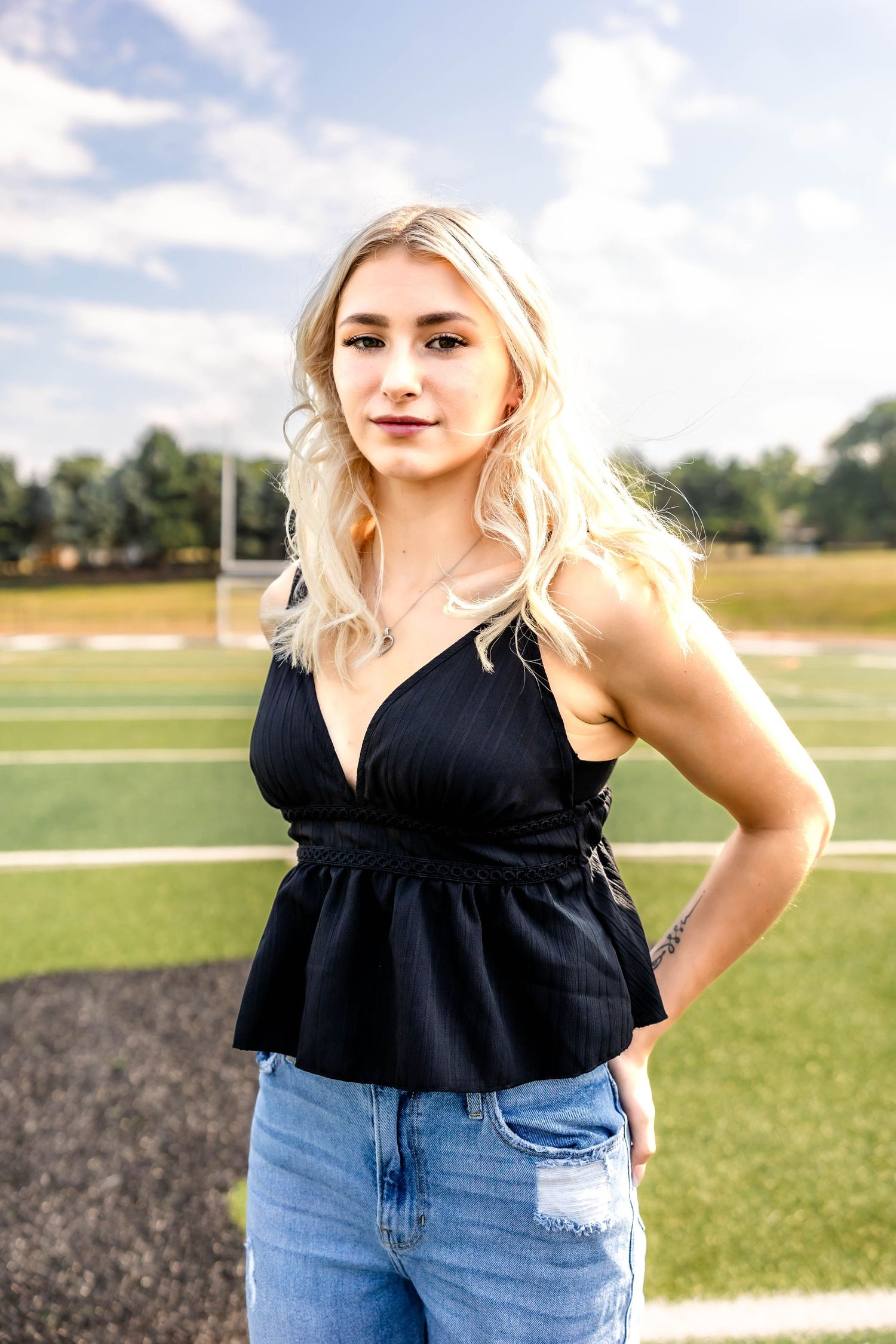 Stylish outfit featuring a black v-neck peplum top paired with light wash denim on an athletic field.