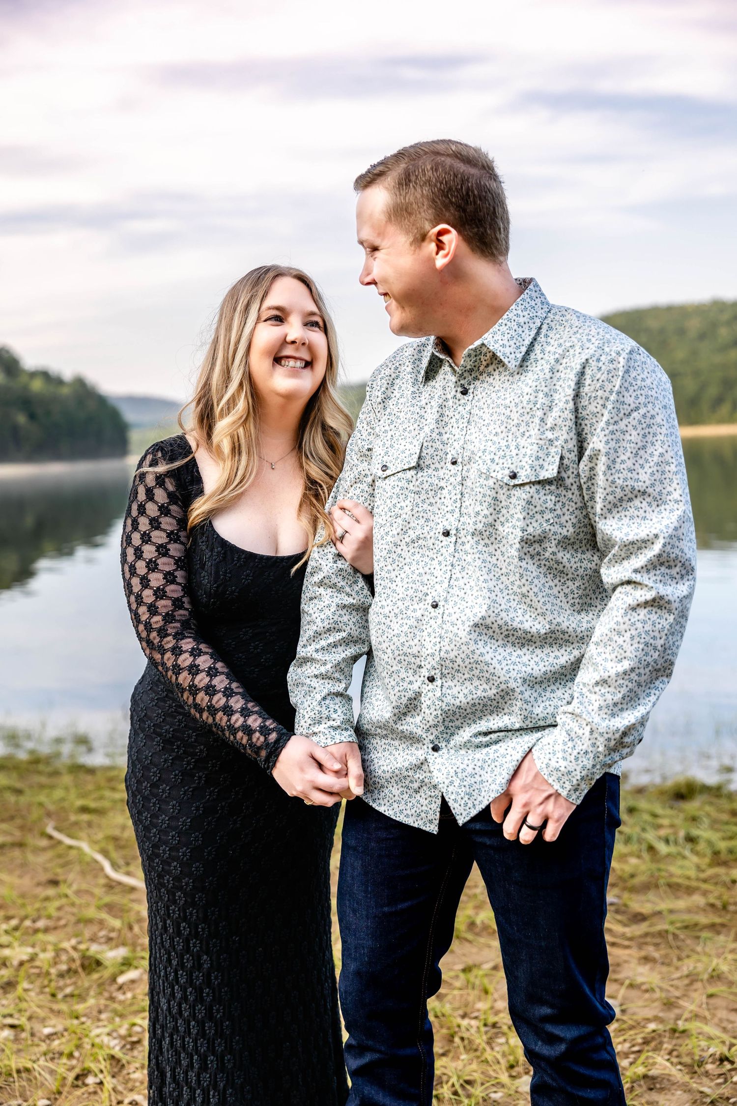Candid moment of couple laughing together near lakeside during engagement session.