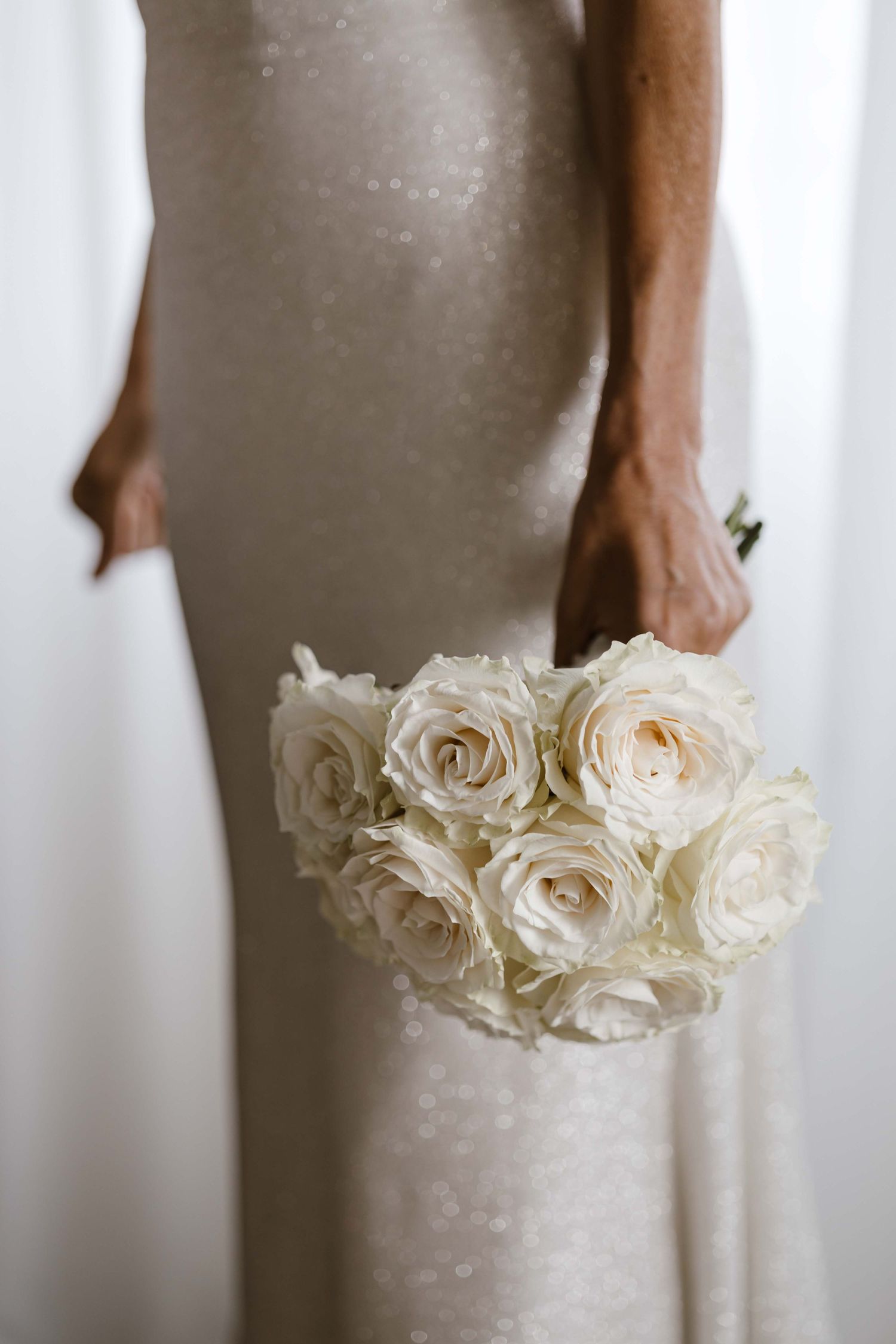 White roses held against a light-colored dress in an elegant bridal bouquet composition.