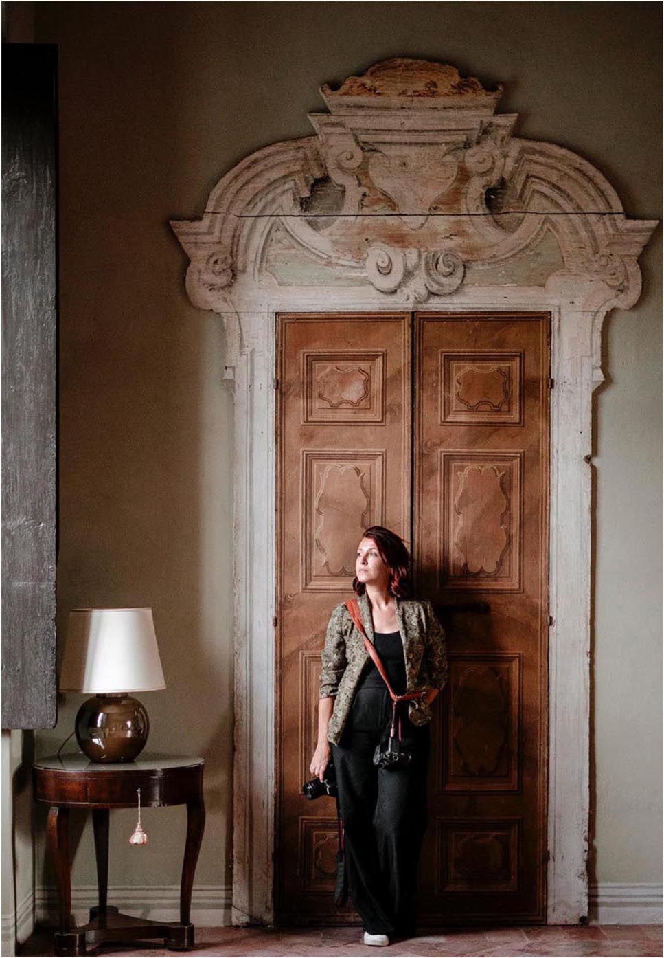 Woman in casual attire standing by an ornate vintage doorway with decorative molding.