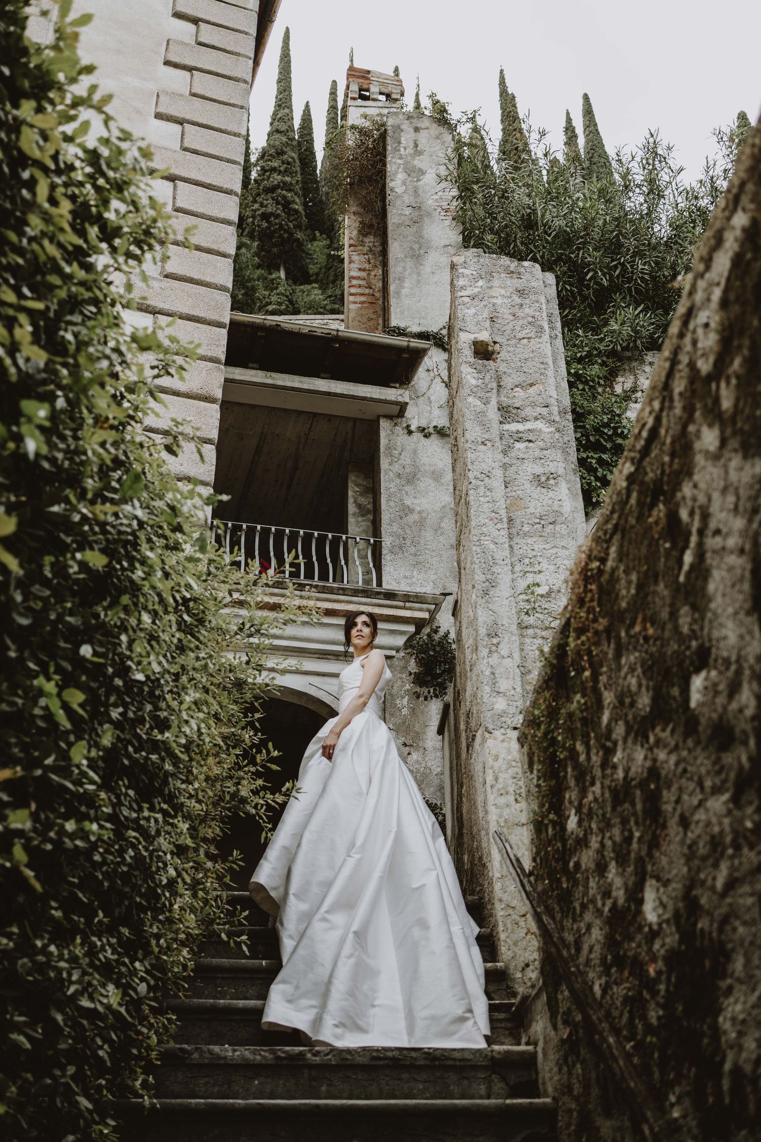Bride in flowing ballgown ascending stone steps at an Italian villa.