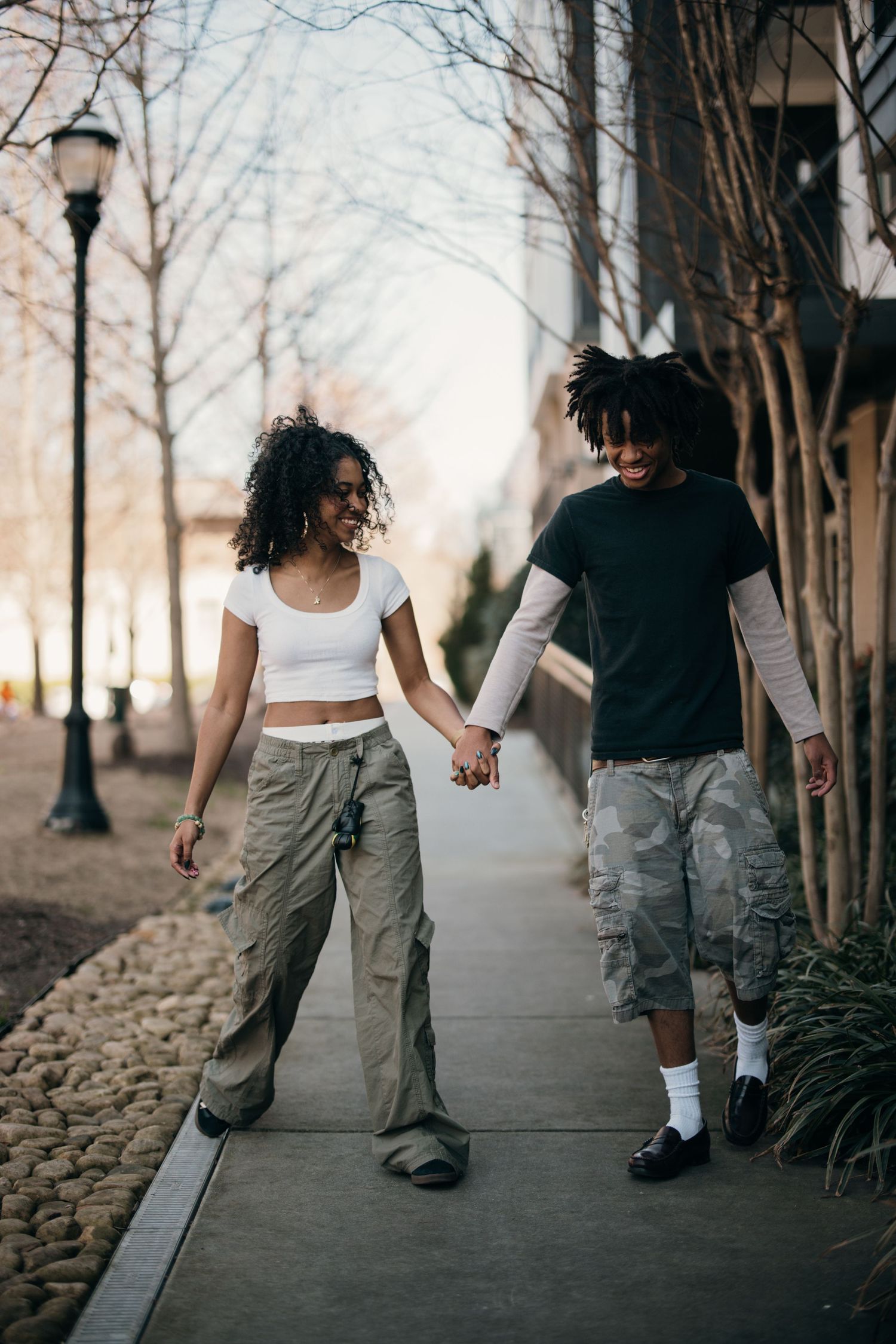 young black couple holding hands, walking down sidewalk lined with trees near Atlantic station, documentary-style couples session Atlanta
