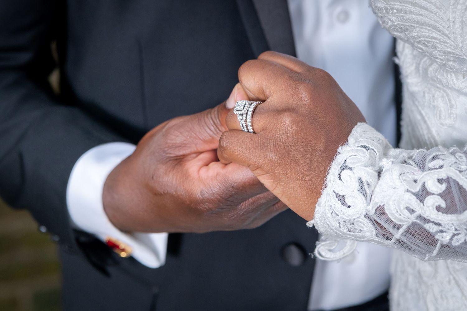 Close-up of hands displaying sparkling diamond engagement ring with lace dress detail.