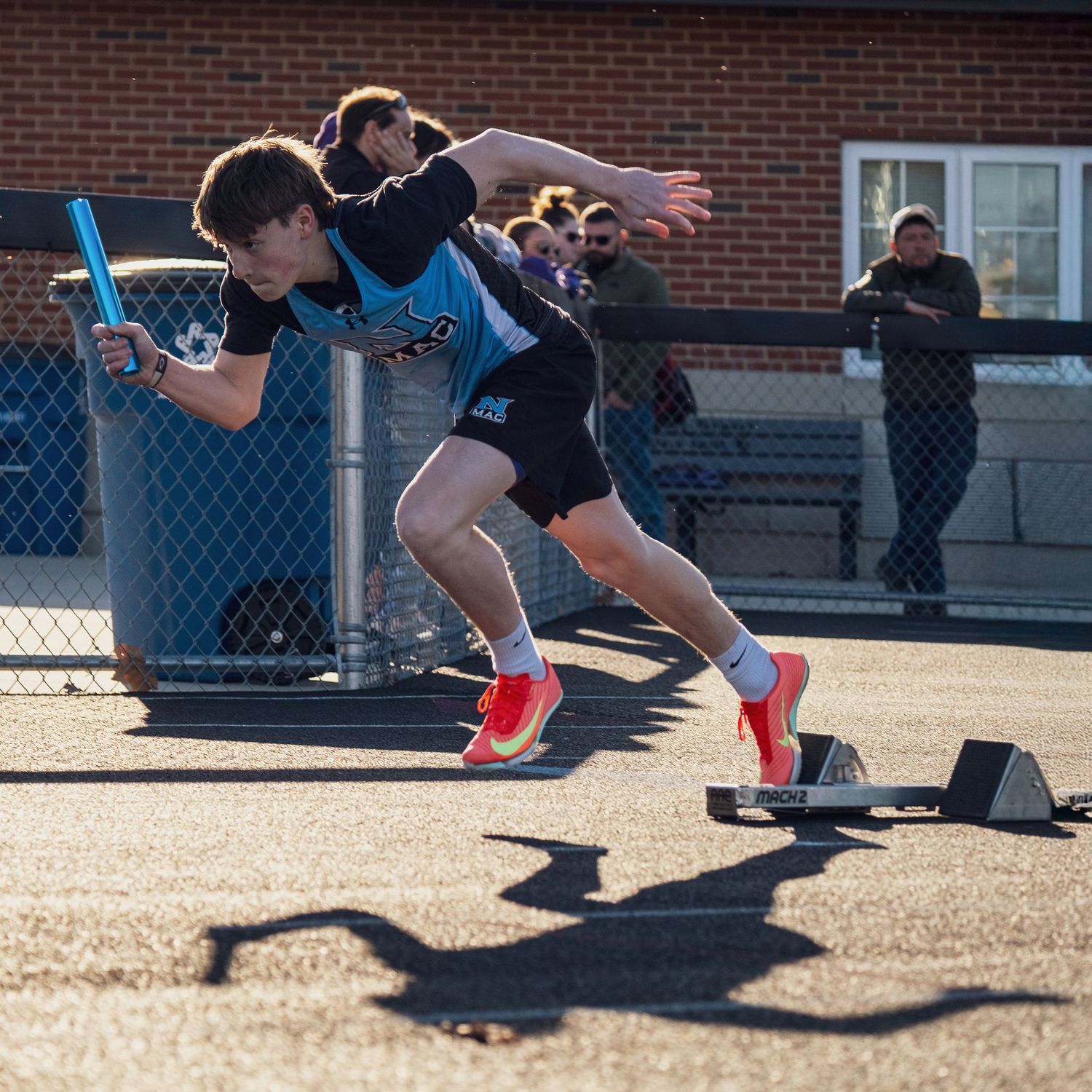 Athletes in blue uniforms burst from starting blocks during track and field practice at a school facility.