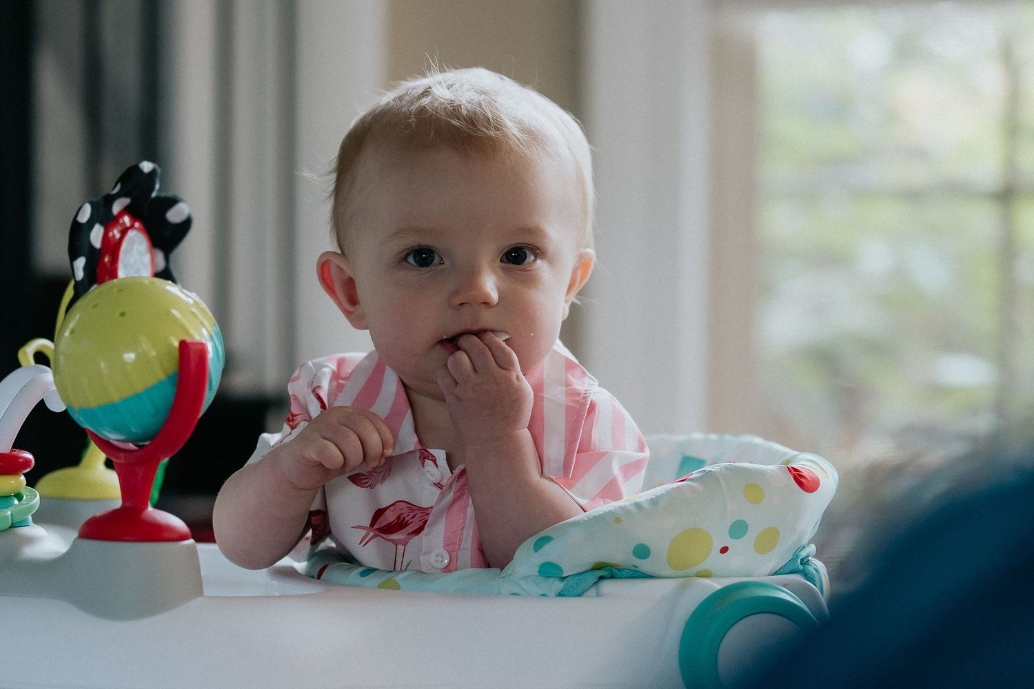 A baby playing during mealtime with colorful toys on a high chair tray.