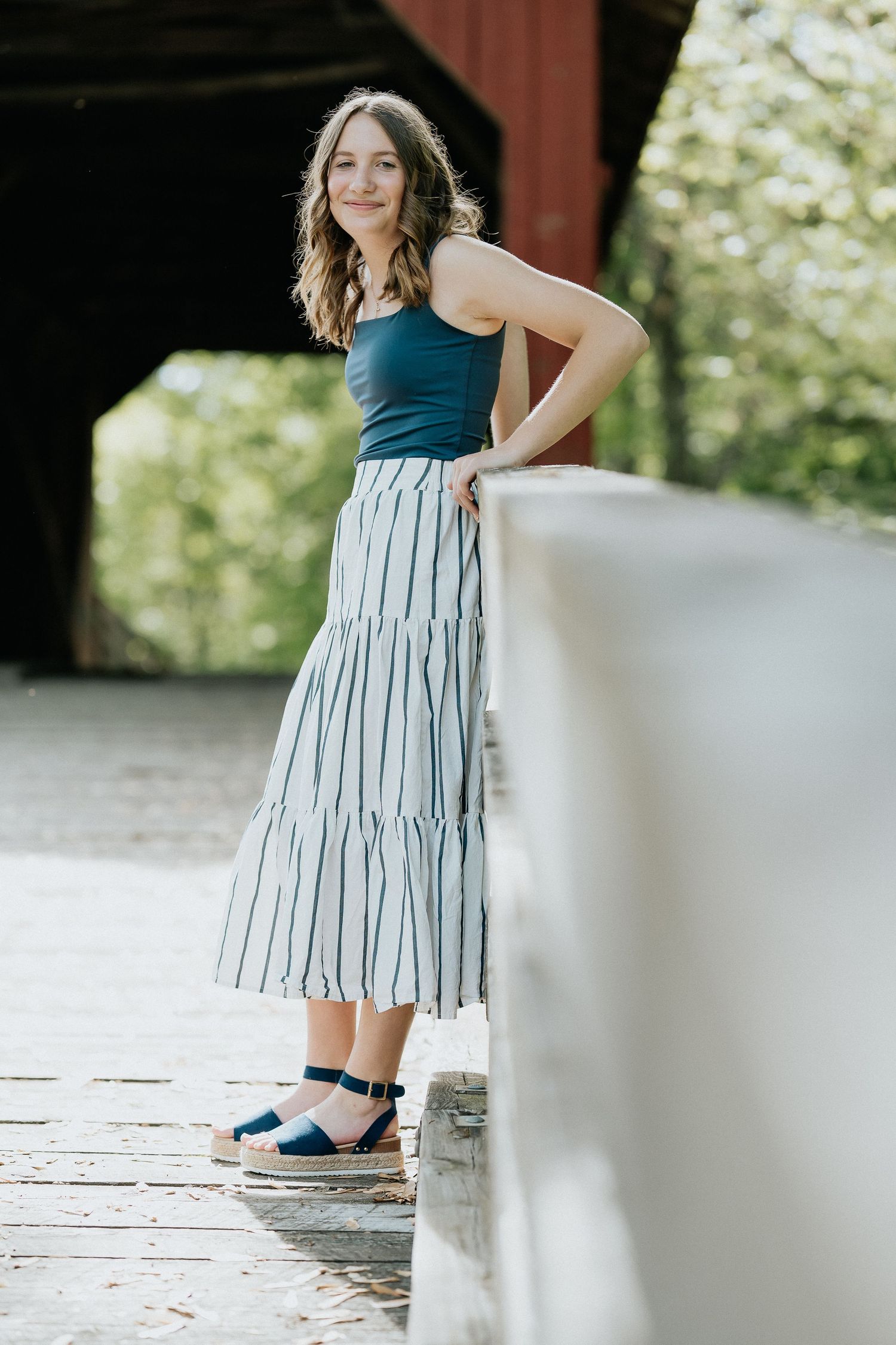 Woman in teal top and striped dress posing in natural outdoor setting.