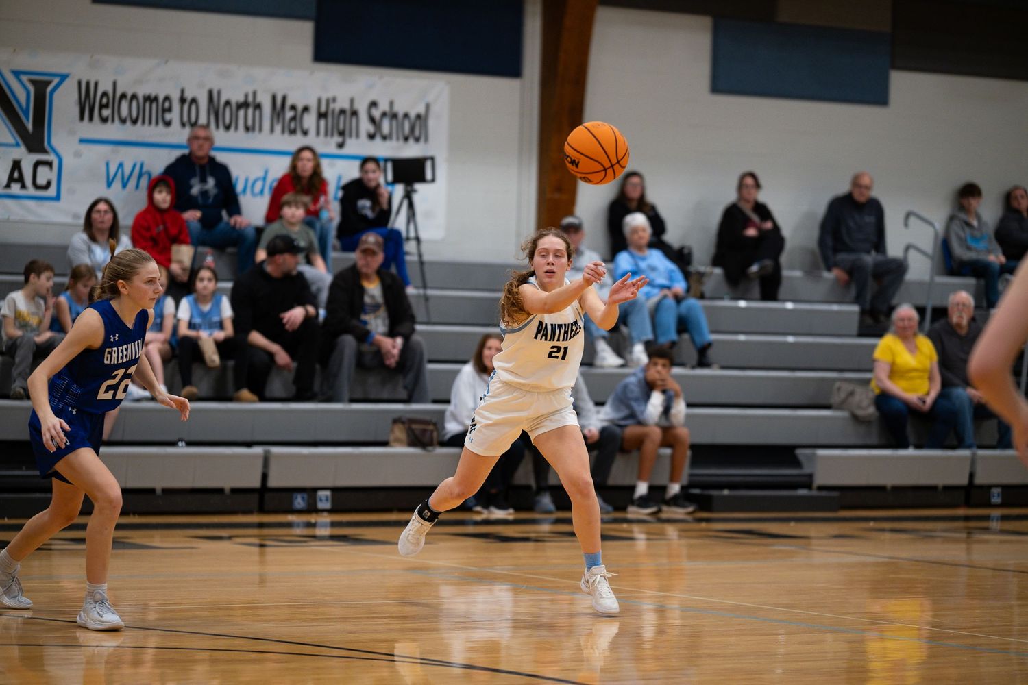 Basketball player in white uniform controls the ball during game against opponents in blue jerseys.