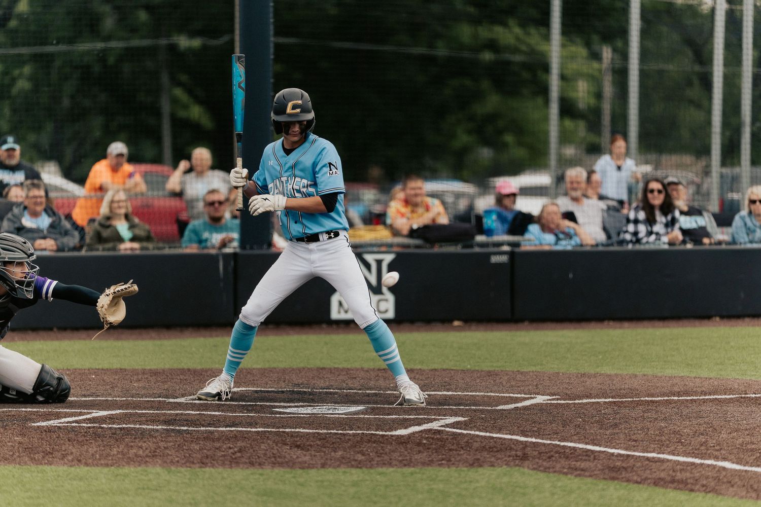 Baseball player in light blue uniform takes batting stance at home plate.