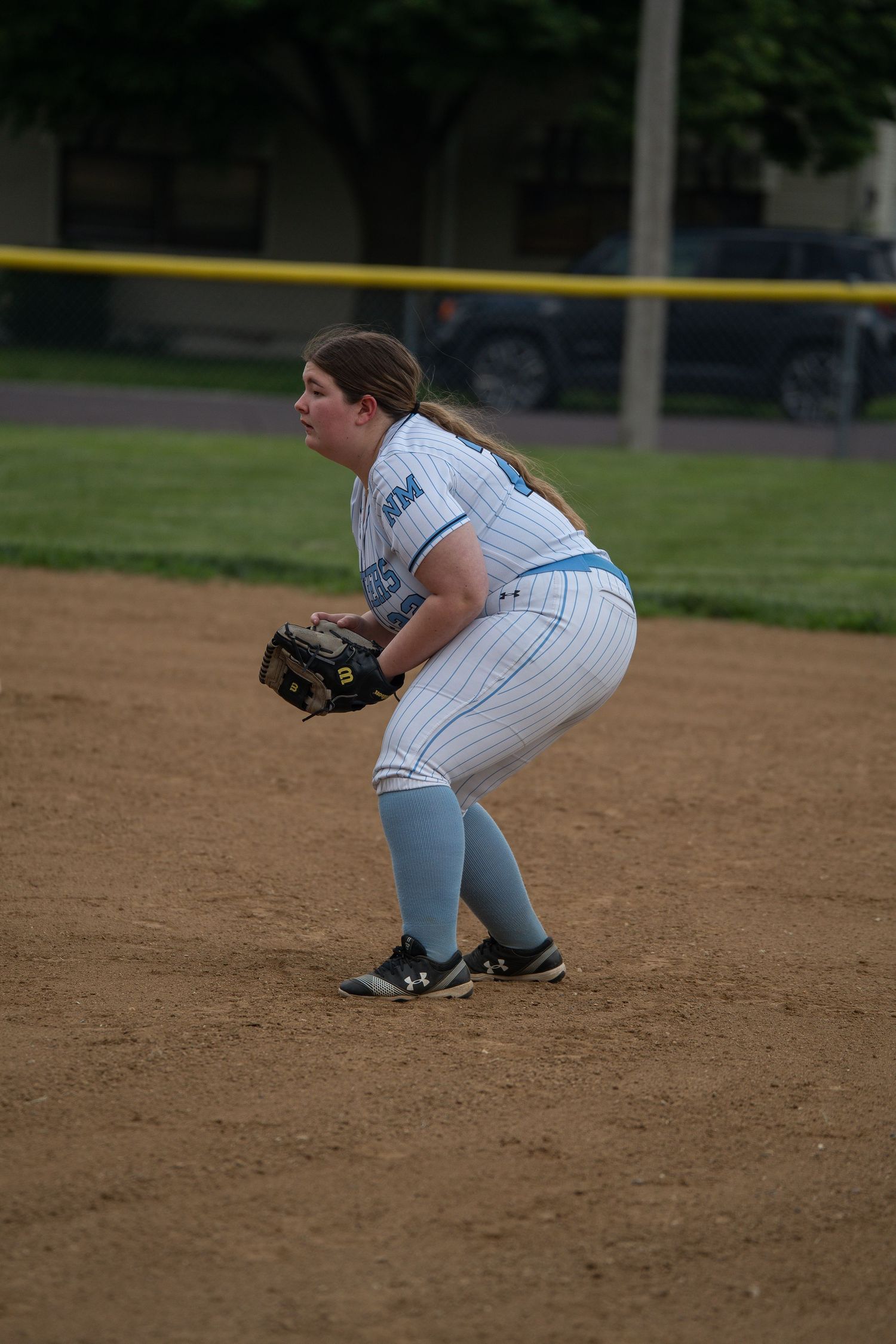 Softball player in pinstripe uniform crouches in ready position on infield dirt.