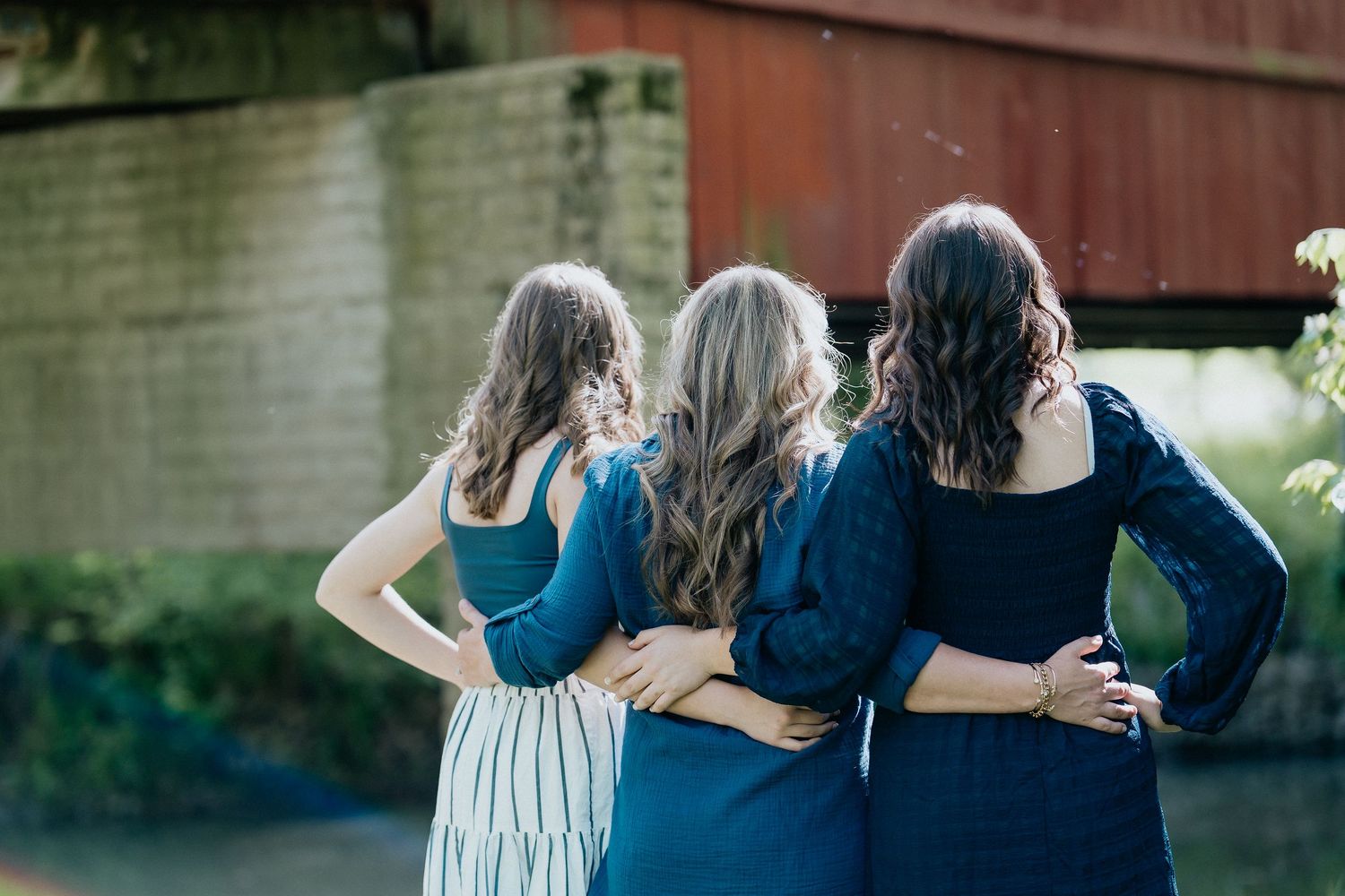 Women in coordinating blue outfits embracing during outdoor photoshoot.