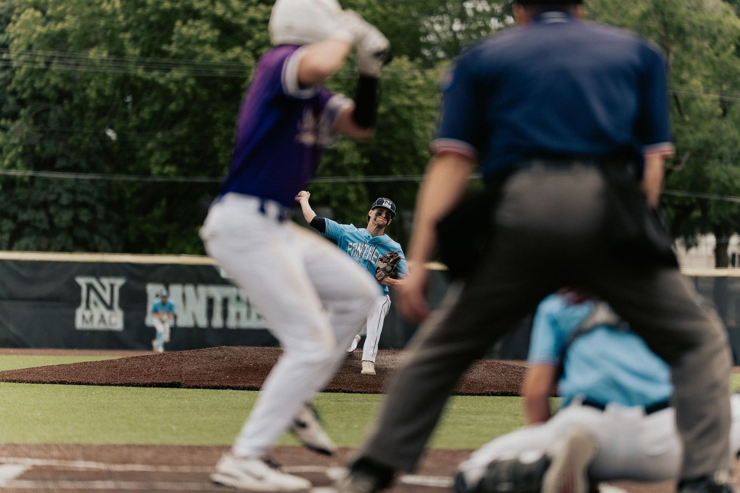 Baseball pitcher in motion on mound with umpire watching during game action.