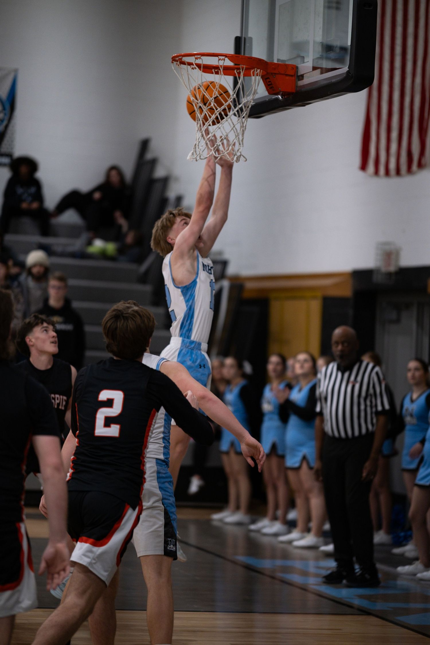Basketball player in light blue jersey attempts a layup against defender in black uniform during indoor game.
