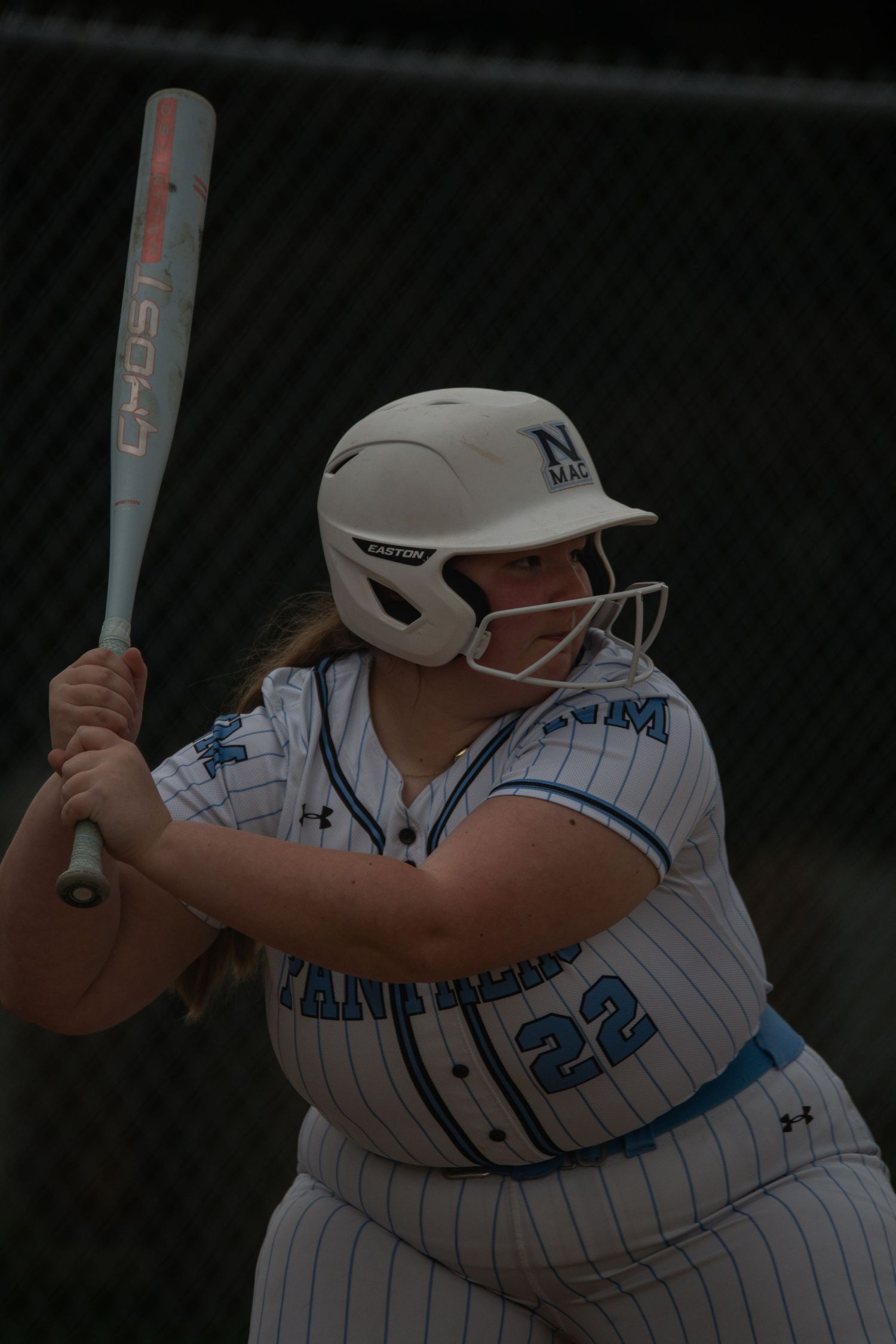 Softball batter in white pinstriped uniform prepares to swing during game.