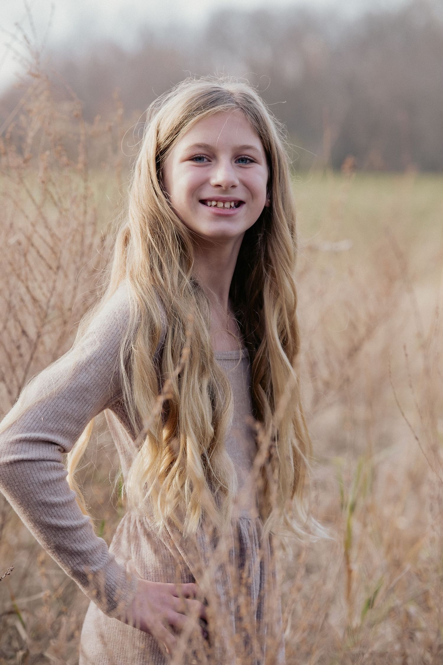 Portrait of a young person with long blonde hair standing in tall grass during golden hour.