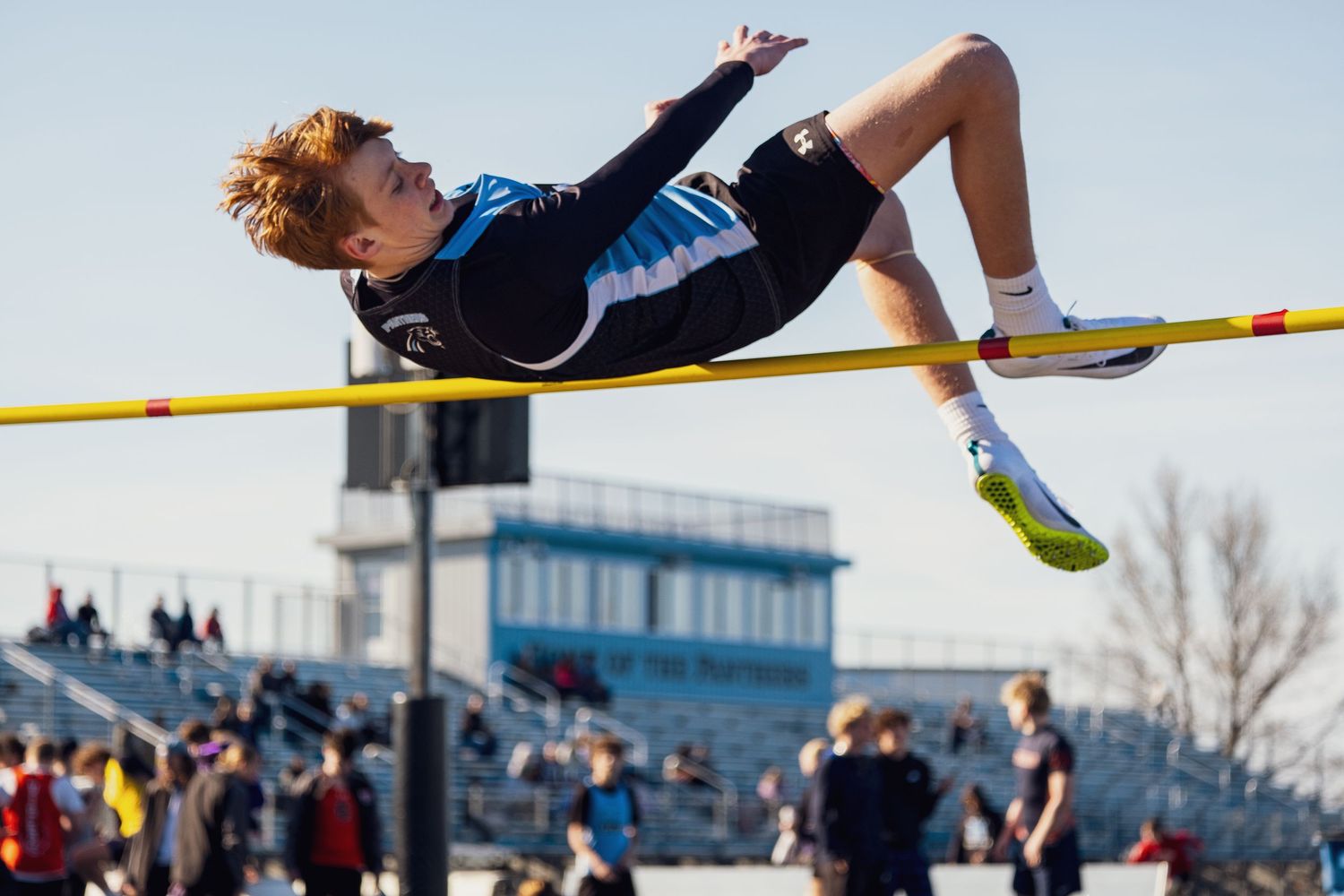 High jumper arches backward over yellow crossbar during track and field competition at outdoor stadium.