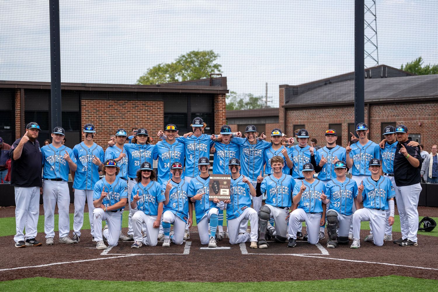 Baseball team in light blue jerseys and white pants posing for group photo on field.