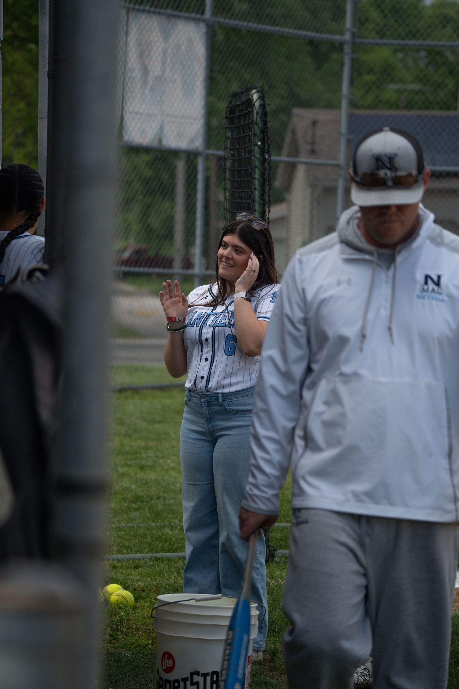 Baseball players in white uniforms standing behind a chain link fence.