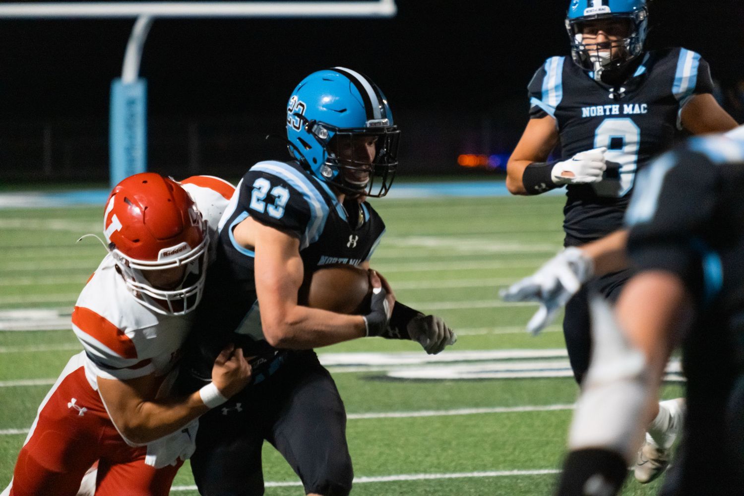 Football players in action during tackle play with blue and orange uniforms.