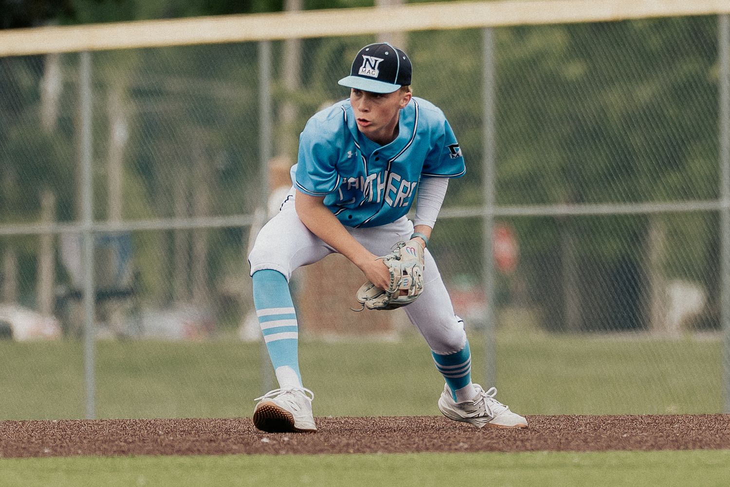 Baseball players in light blue uniforms positioned on the infield dirt.