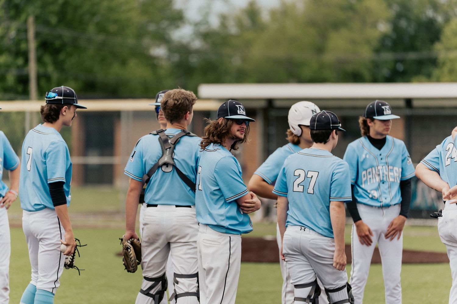 Baseball team huddles together wearing light blue uniforms during game discussion.