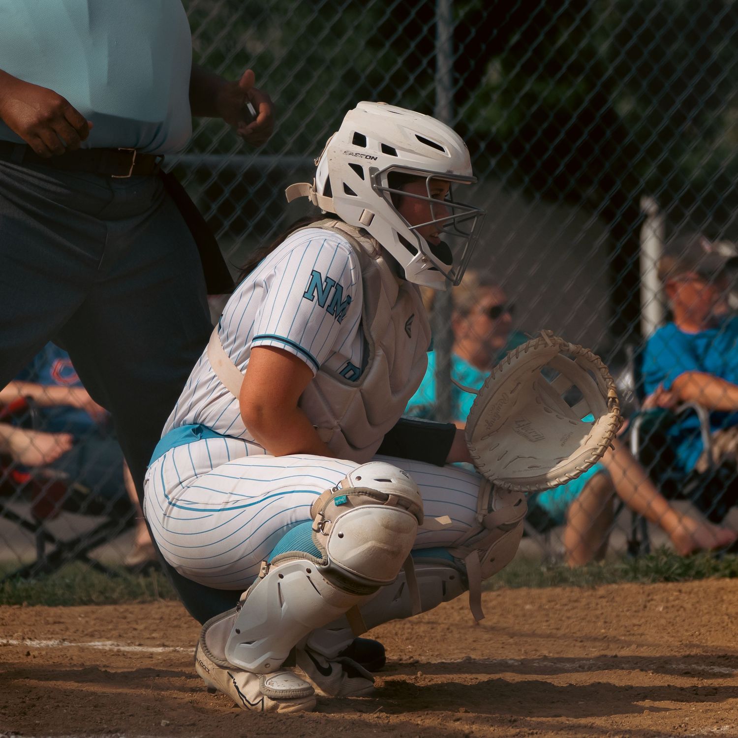 Baseball catcher in blue and white uniform crouches behind home plate during a game.