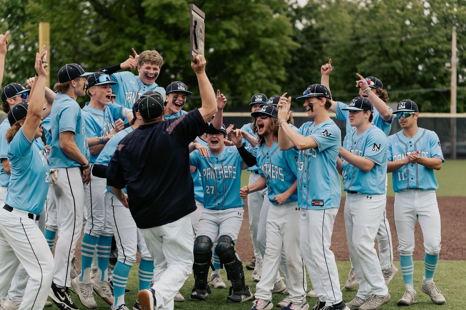 Baseball team in light blue uniforms celebrates a victory together on the field.