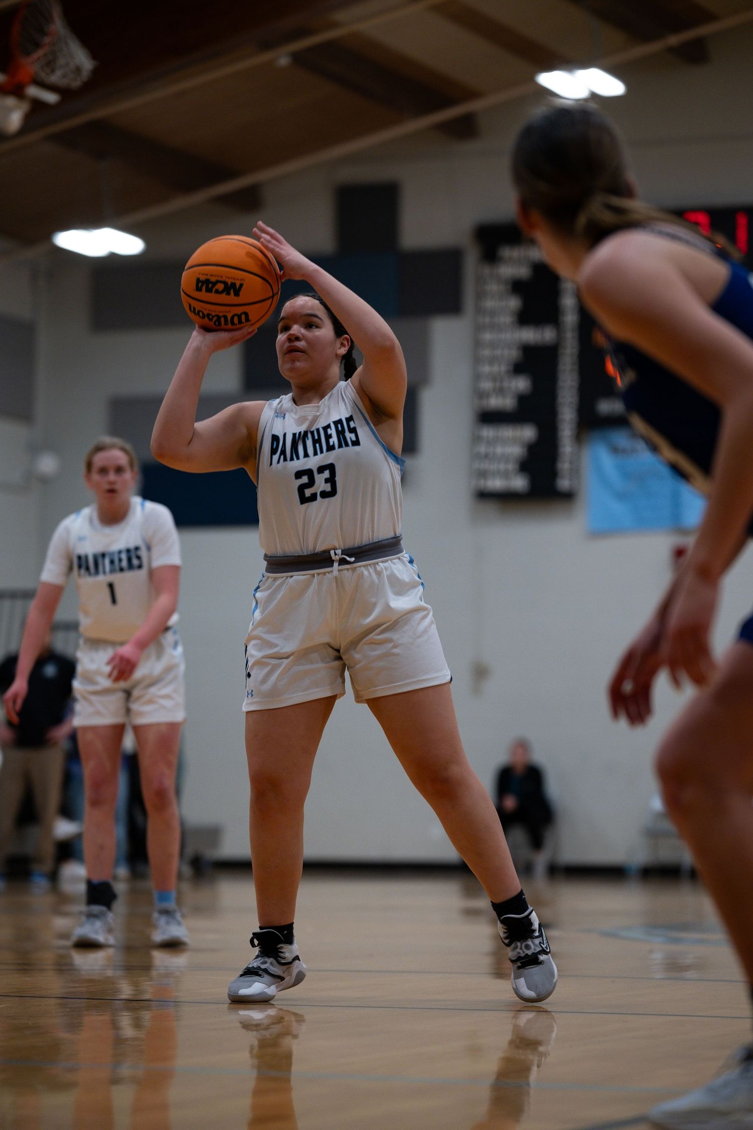 Basketball player wearing white number 23 jersey takes a shot during indoor basketball game at school gymnasium.