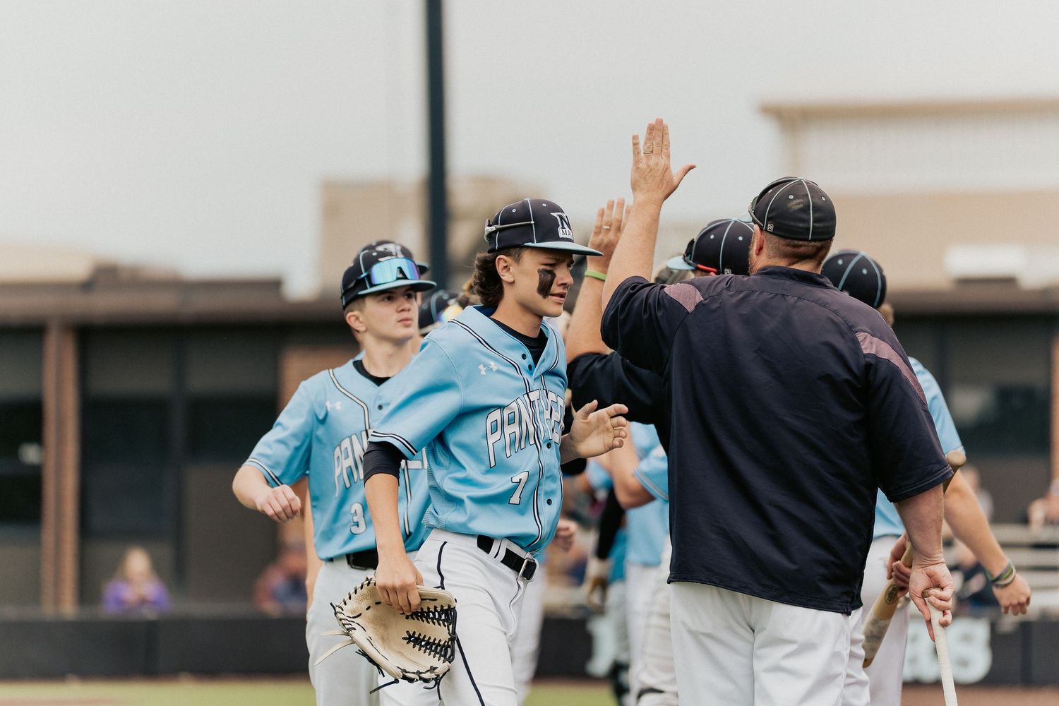 Baseball team celebrating with high fives after scoring a run.