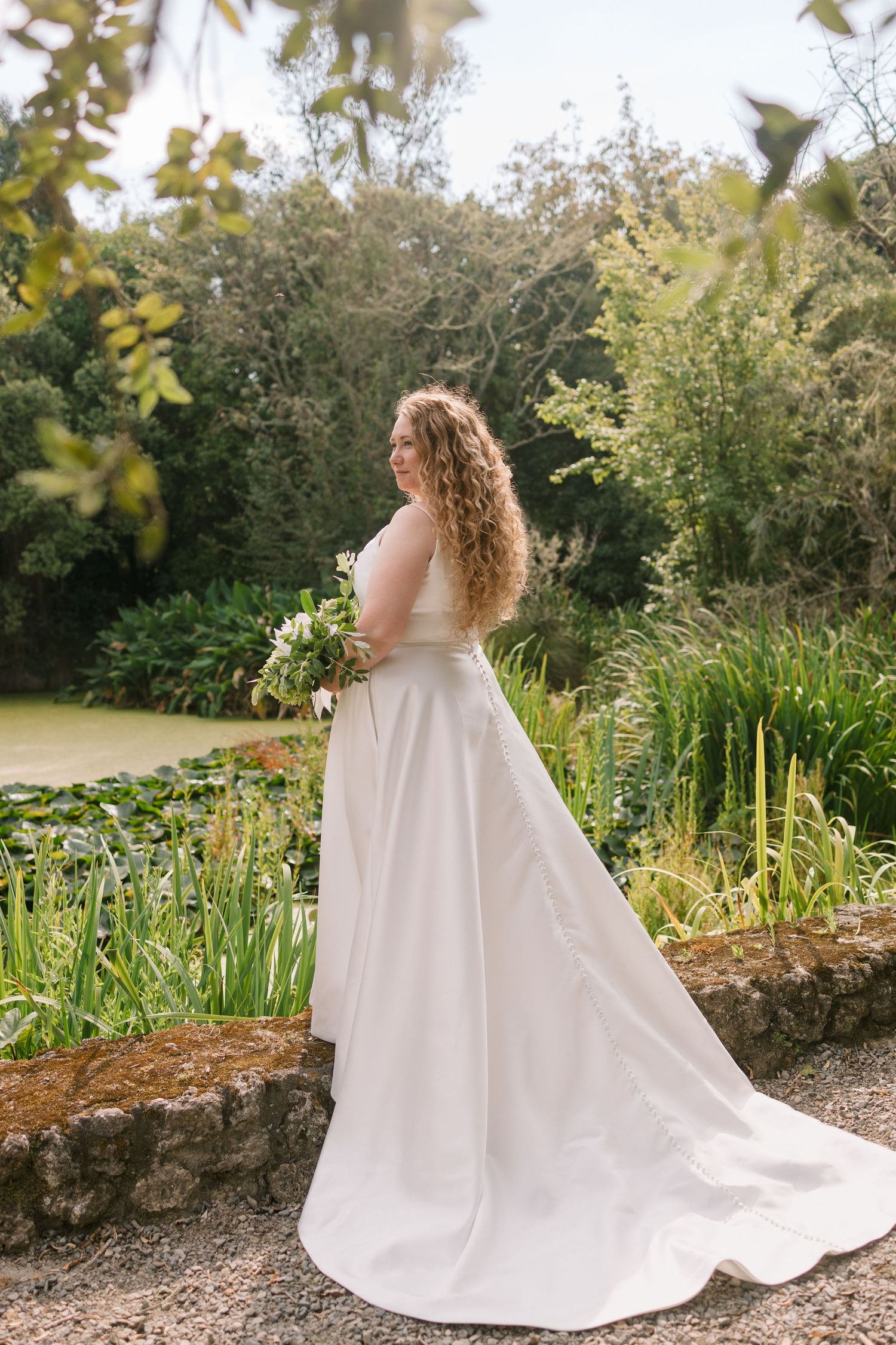 Bride in flowing white gown poses in lush garden setting.