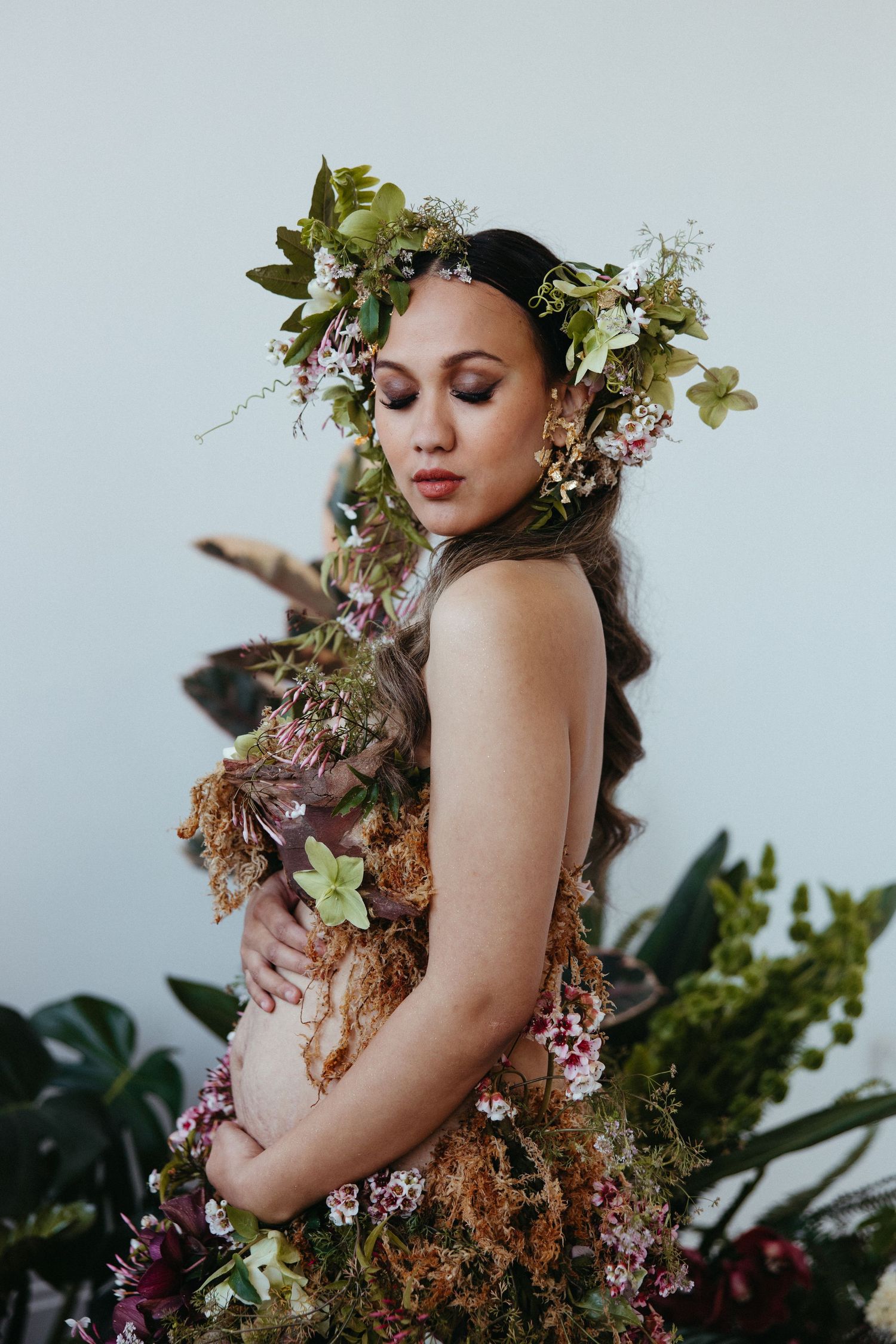 Ethereal fashion portrait featuring a floral crown, delicate florals, and natural greenery against a light background.