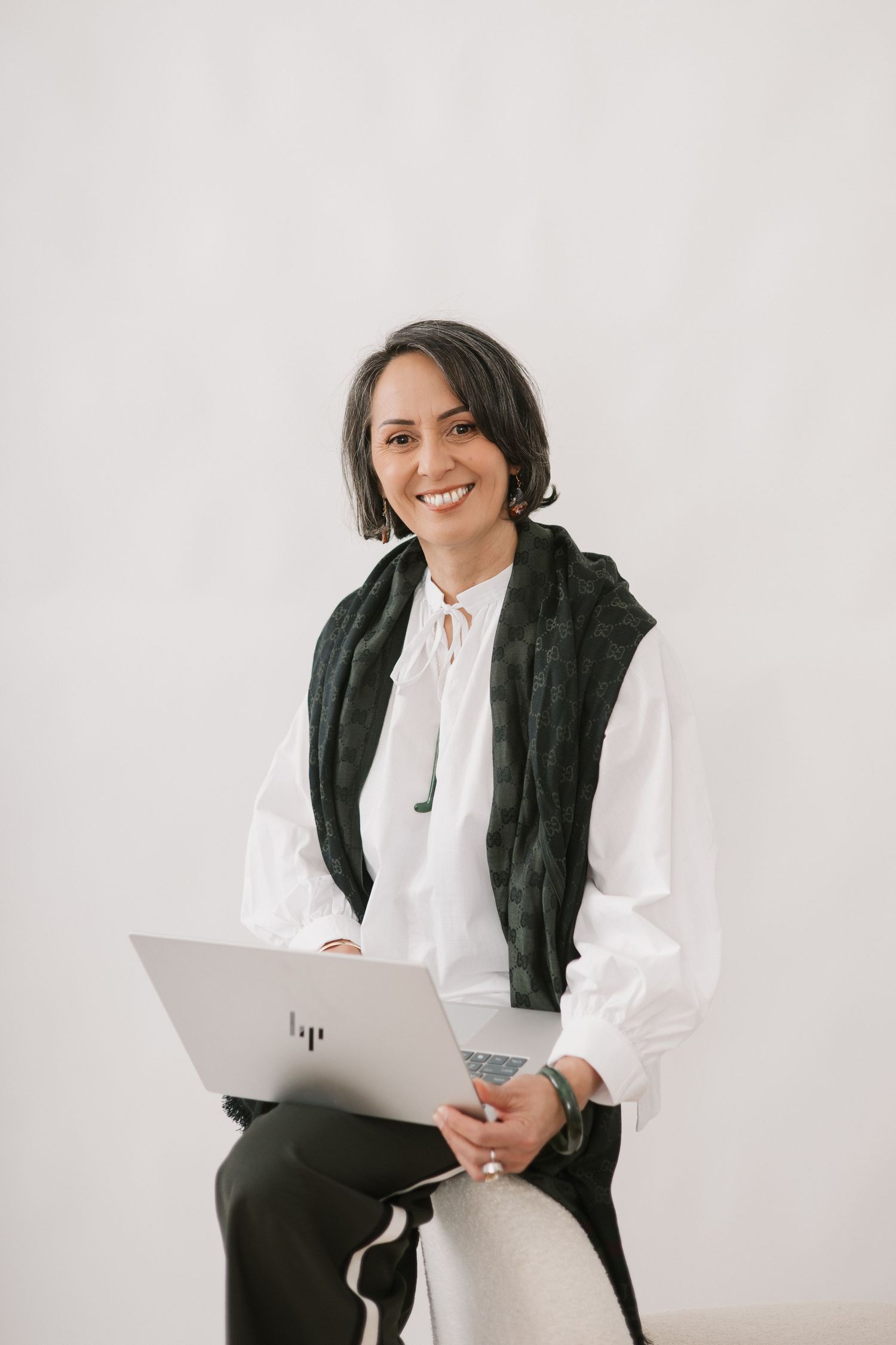 Professional wearing a white blouse and dark vest sits with laptop against white background.