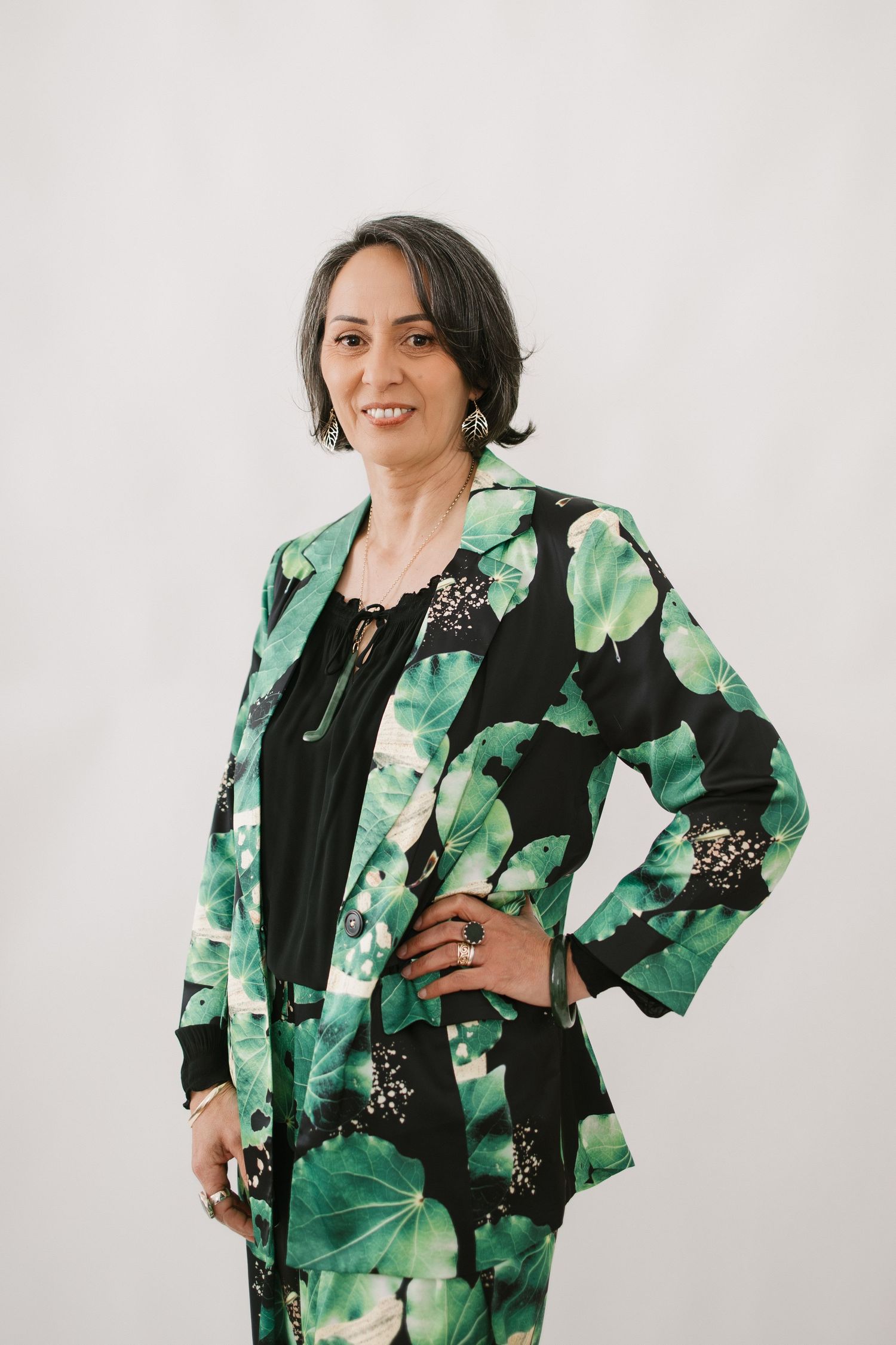 Professional studio portrait showing someone wearing a stylish black and green floral print blazer against a light background.
