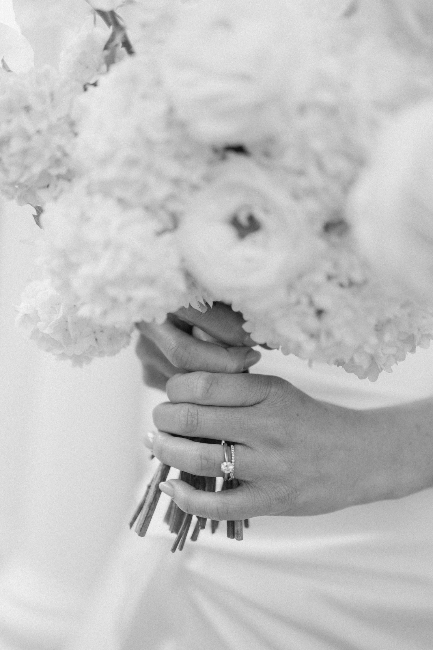 Close-up of bride's hands holding white hydrangea bouquet with engagement ring visible.