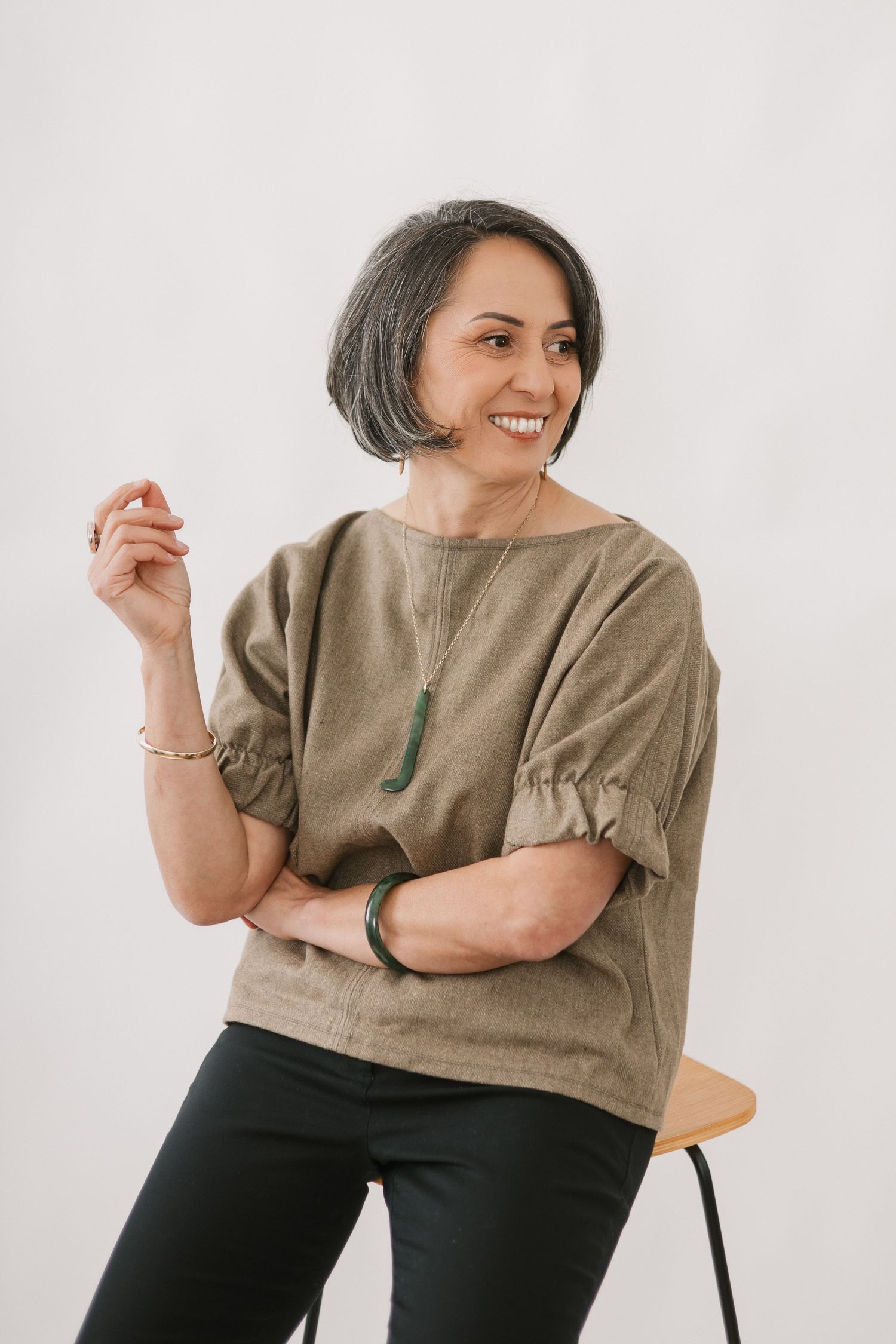 Woman in beige linen top and dark pants smiles while posing against white background in casual lifestyle photos.