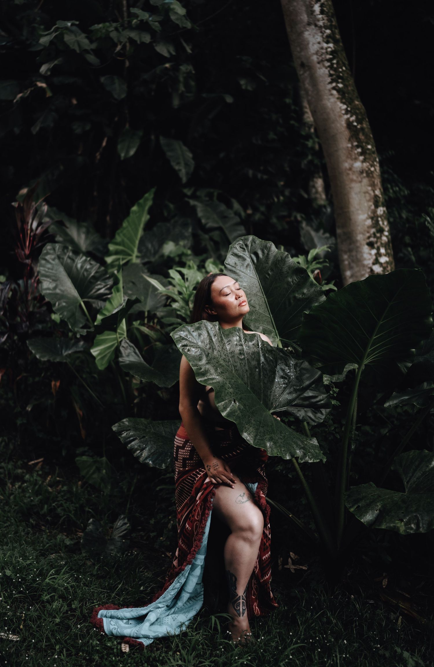 Artistic portrait in a lush tropical garden setting with giant elephant ear leaves creating a dramatic natural backdrop.