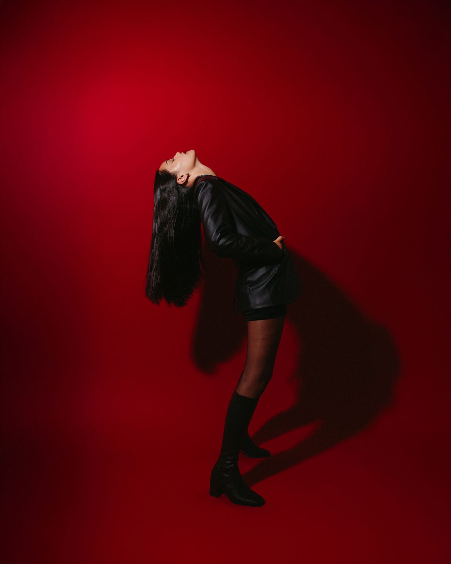 Dramatic silhouette in black outfit against deep red background bending backwards with flowing dark hair.