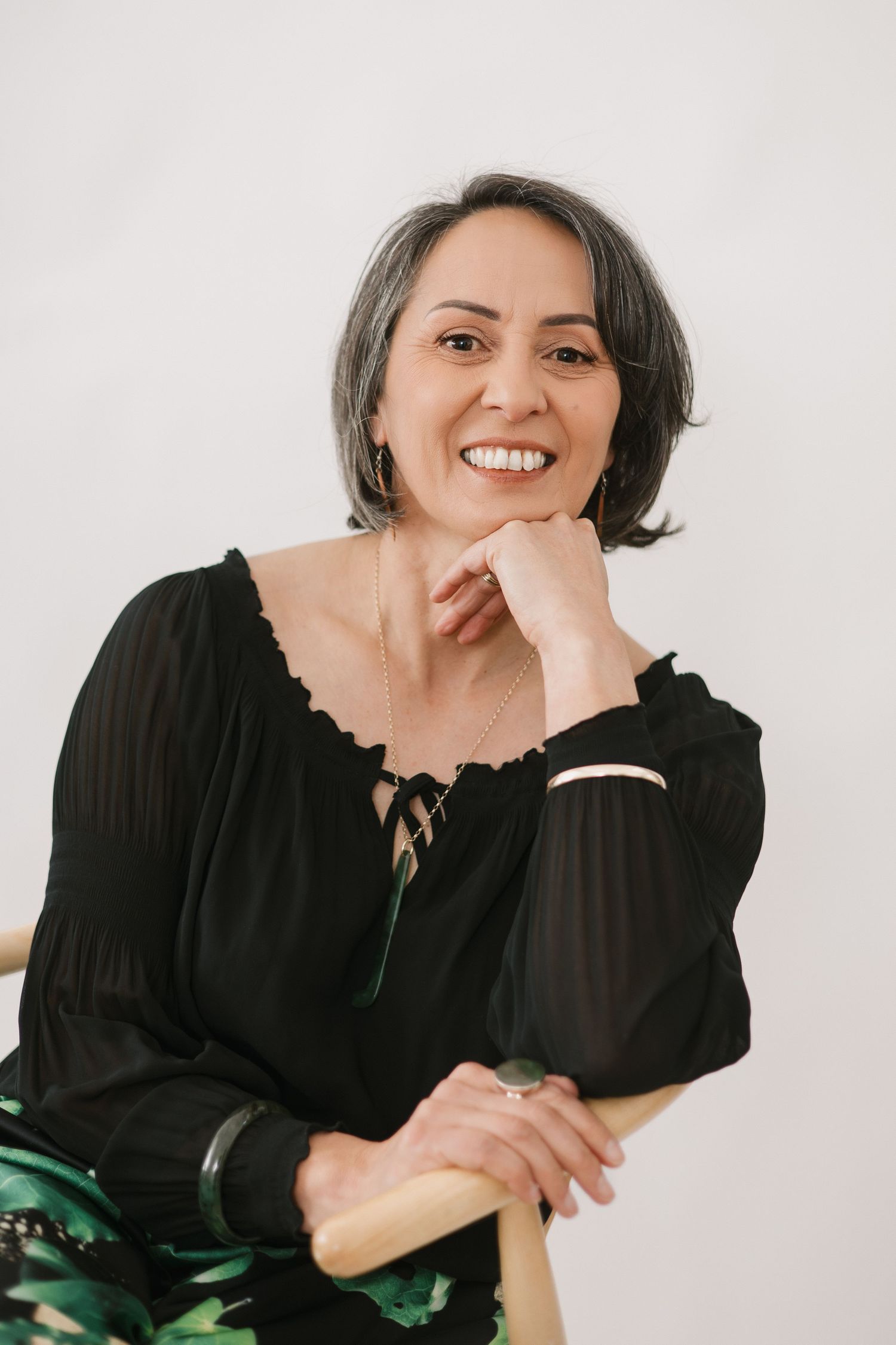 Professional portrait against white background showing bright smile and black peasant blouse with long sleeves.