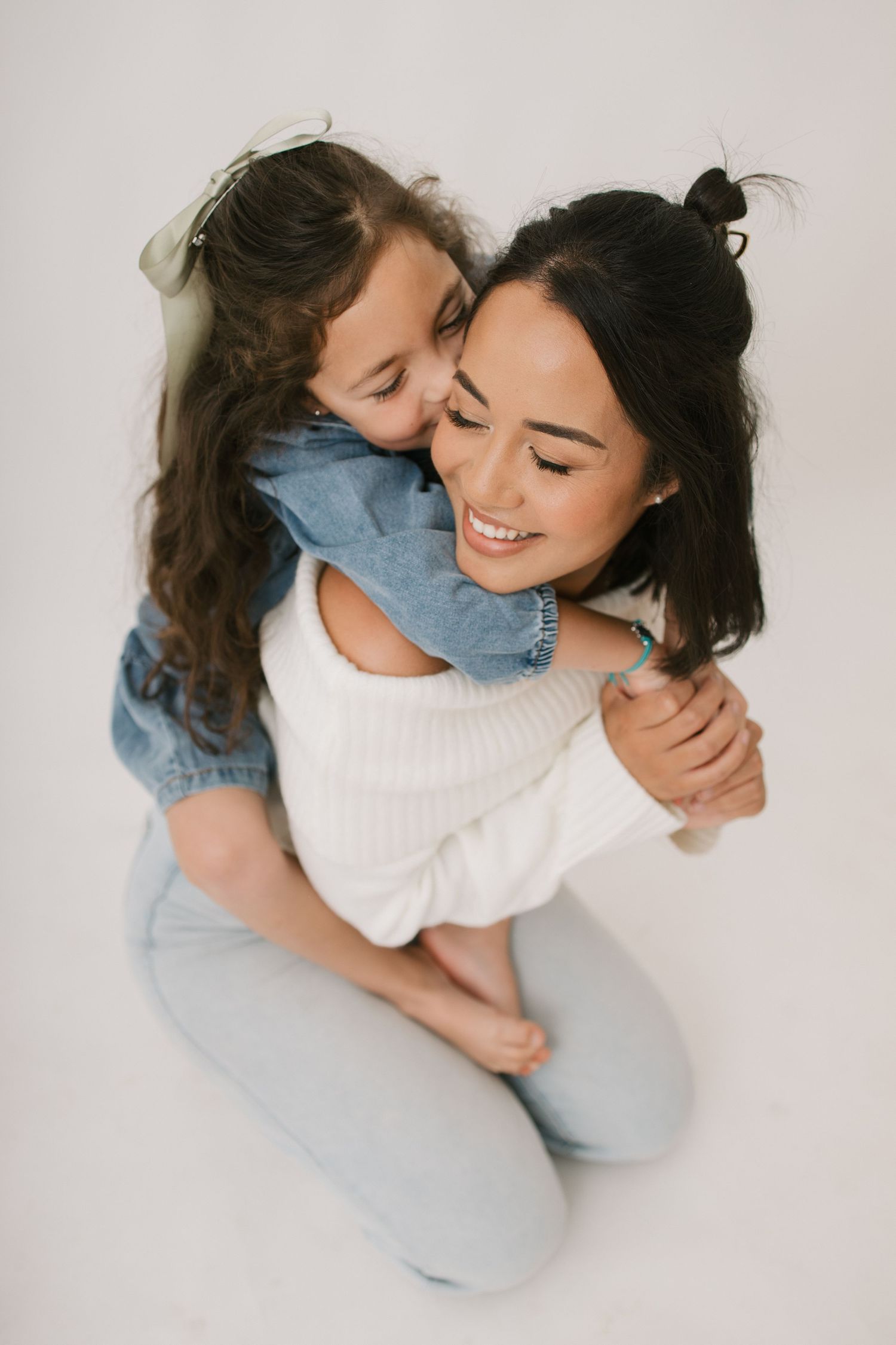 A tender moment between mother and child sharing an embrace while sitting on a white background.