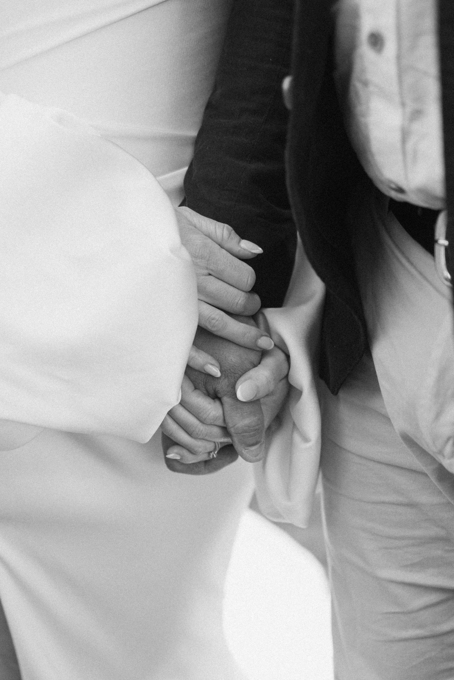 Close-up black and white photo of couple holding hands during wedding ceremony.