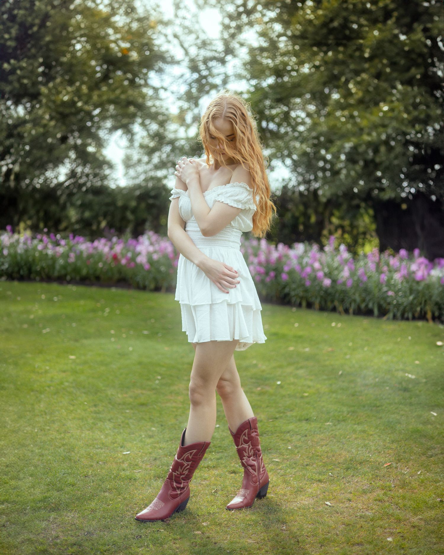 Person in a white summer dress and brown cowboy boots standing in a garden with purple wildflowers in the background.