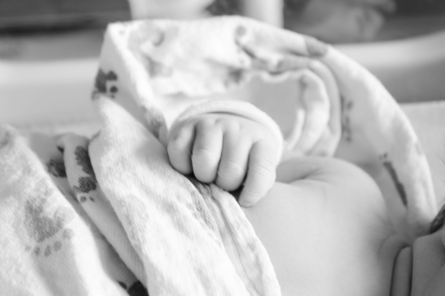 Black and white close-up of newborn's tiny hand grasping blanket.
