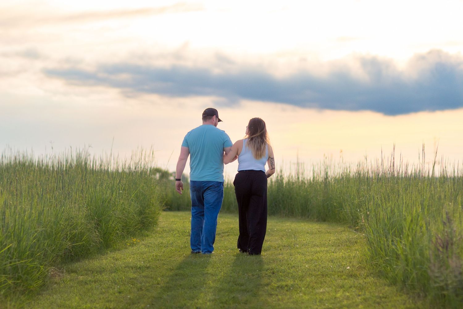 Two people walking together along a grassy ridge at sunset against a dramatic cloudy sky.
