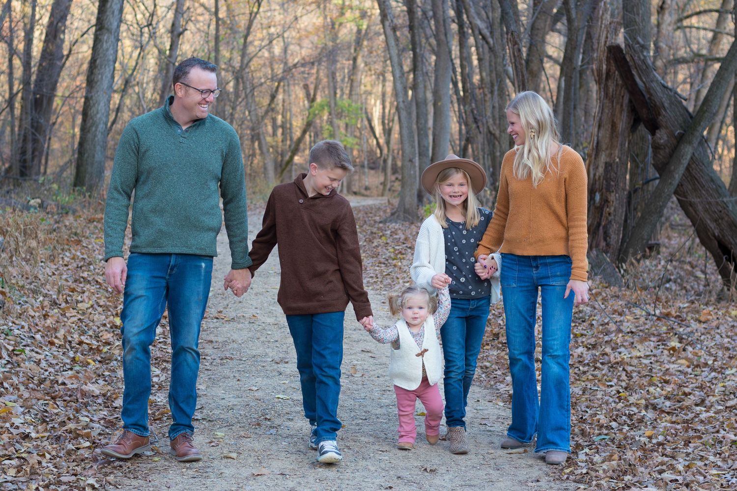 A group of people walk together on a path through autumn woods with fallen leaves scattered on the ground.