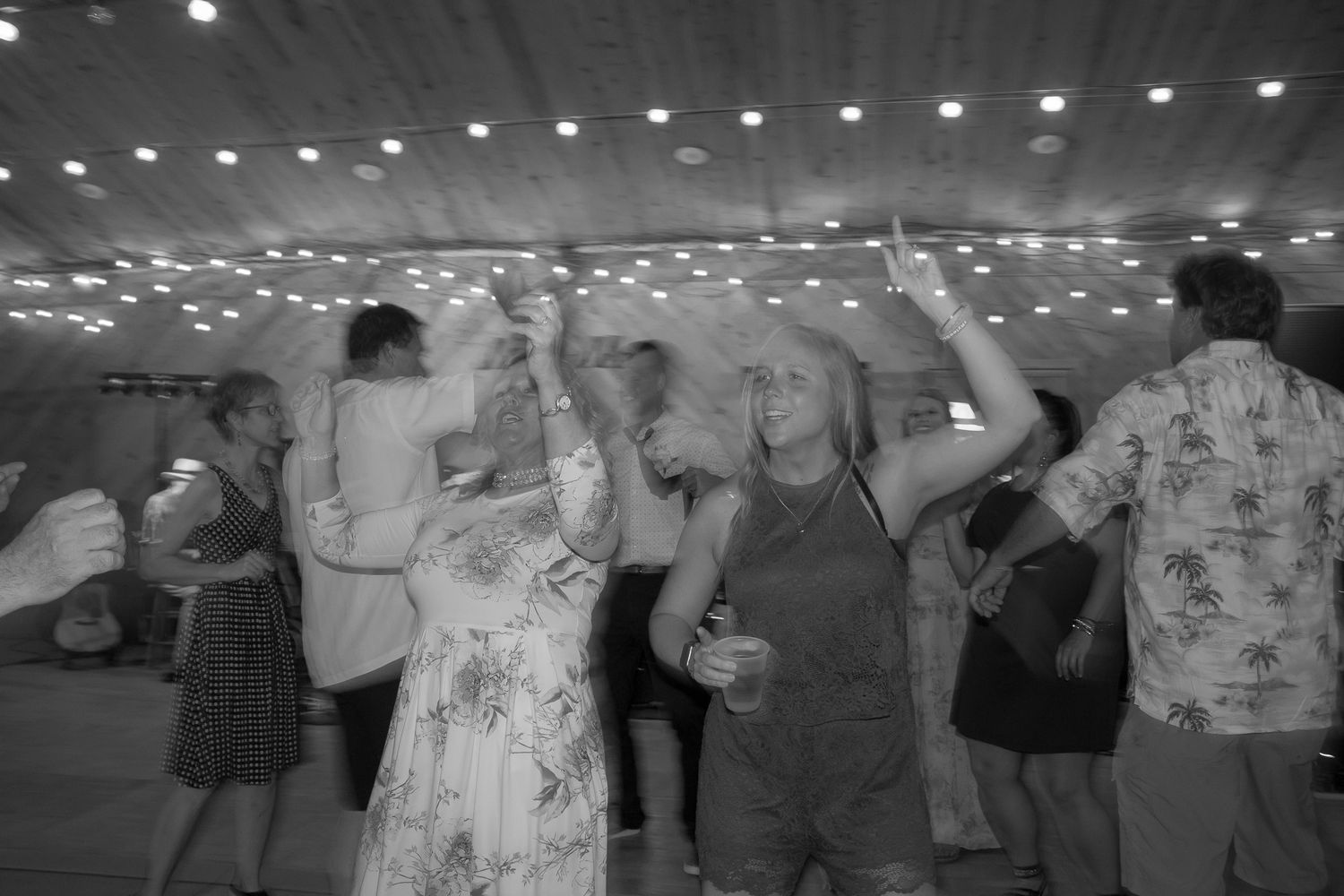 Black and white photo of dancing guests under string lights at a wedding reception.
