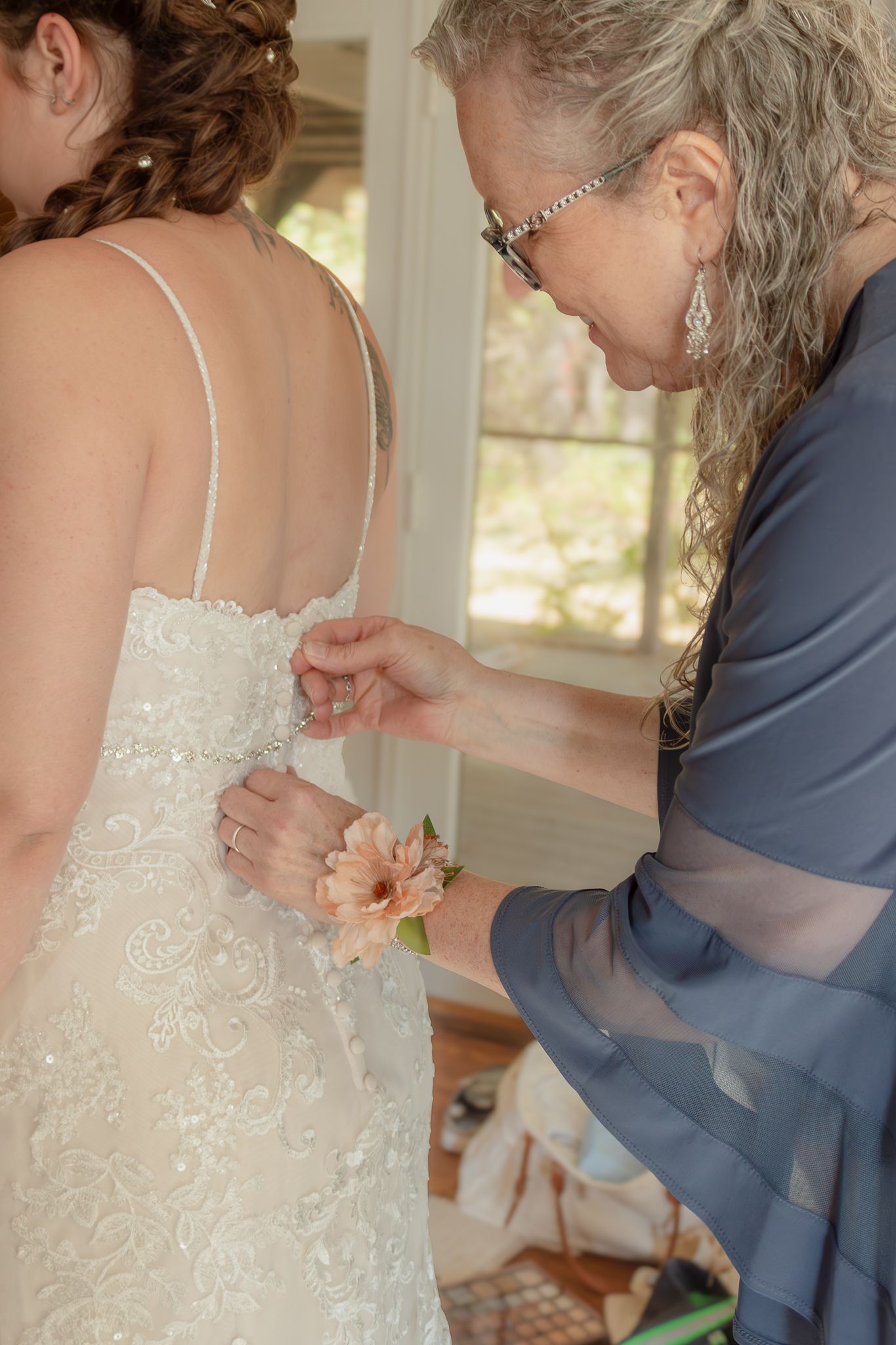 A close-up of someone helping with the final touches on a lace wedding dress.