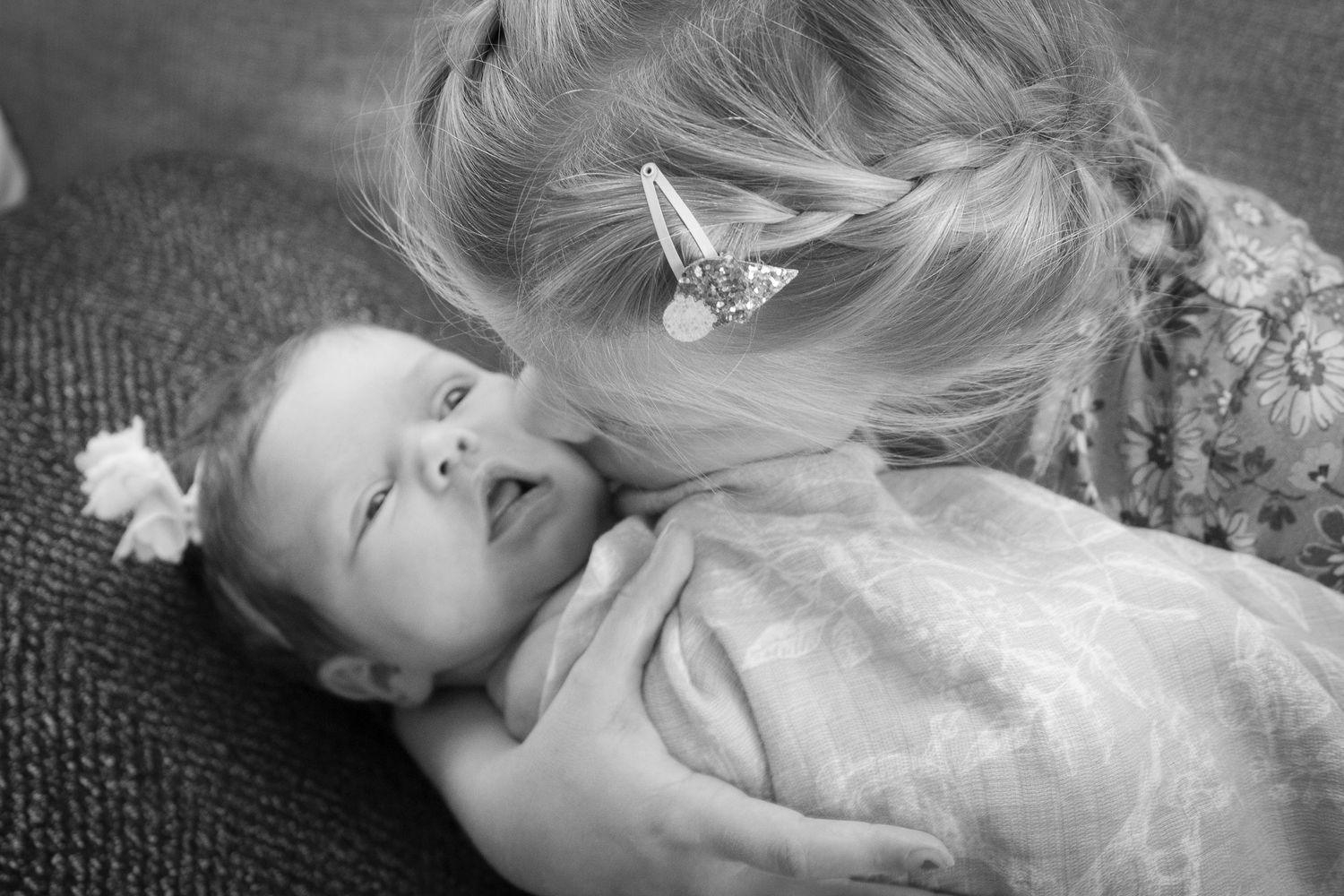 Black and white intimate moment between parent and baby on grey surface.