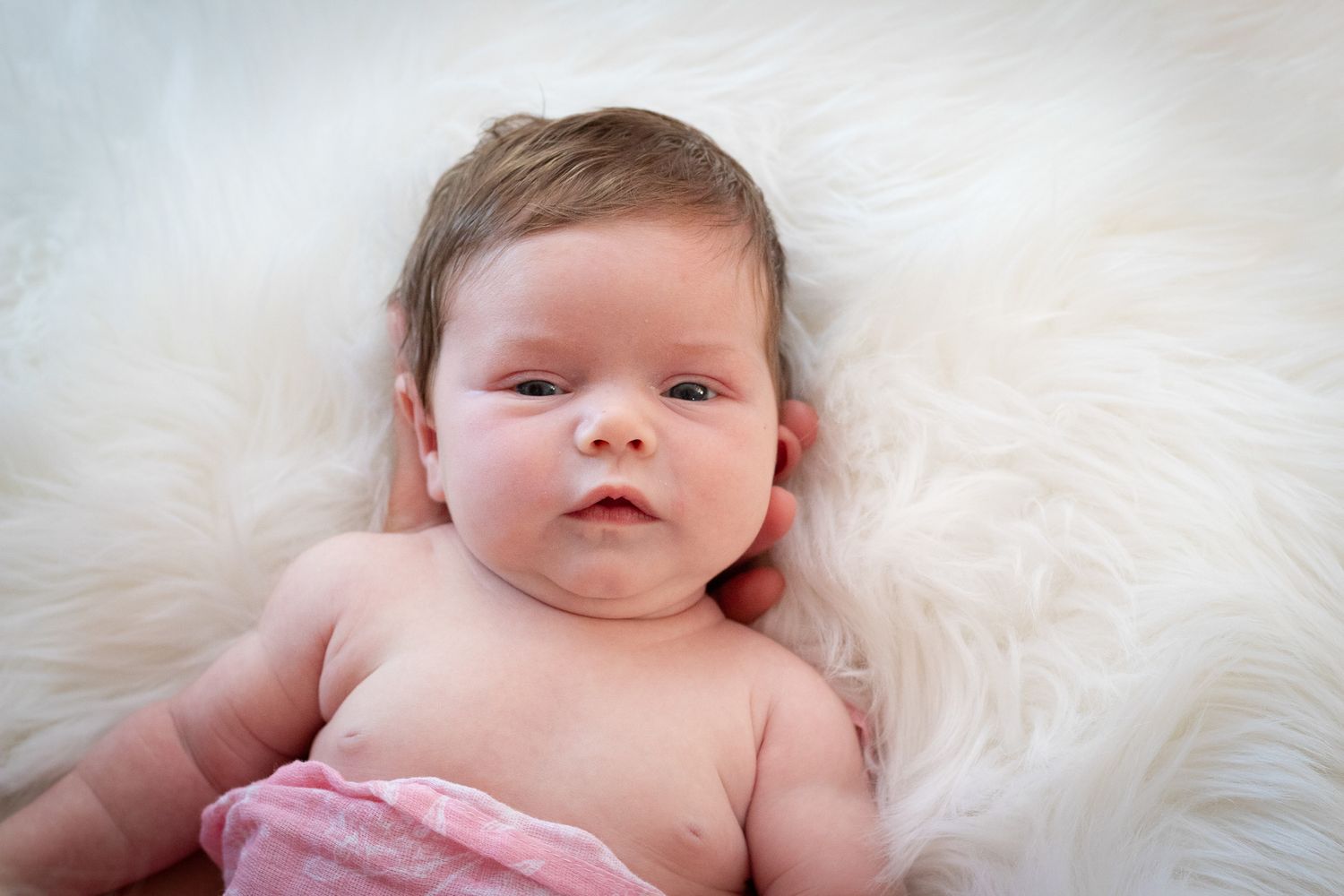 Baby resting on white furry blanket with rosy cheeks.