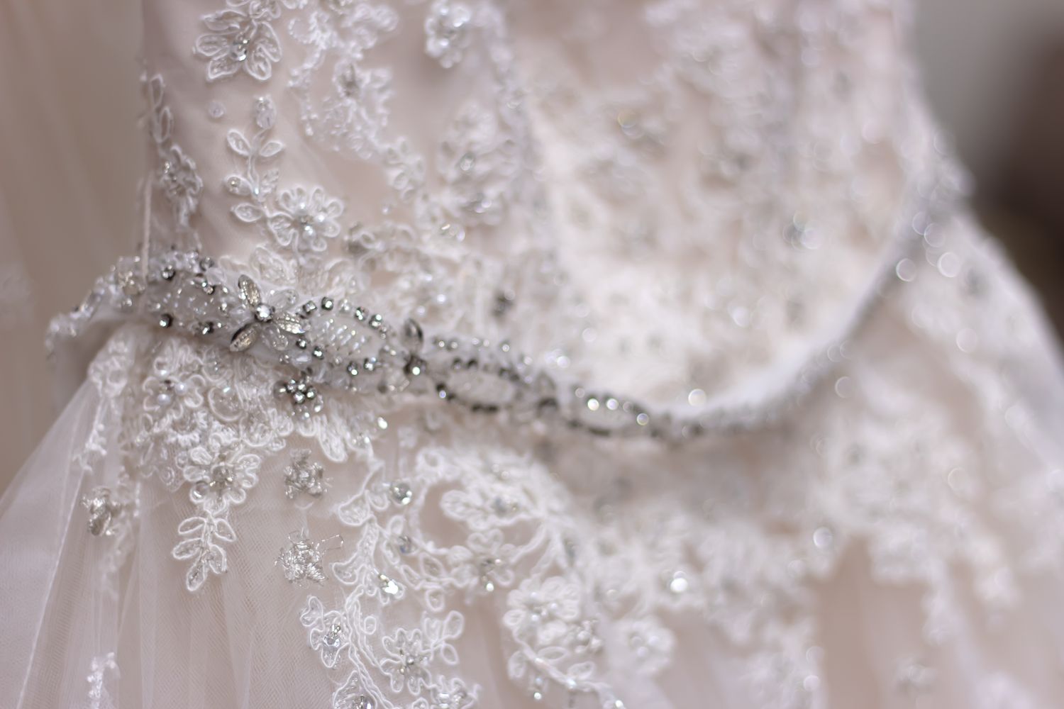 Close-up detail of intricate white lace and beading on a wedding dress.