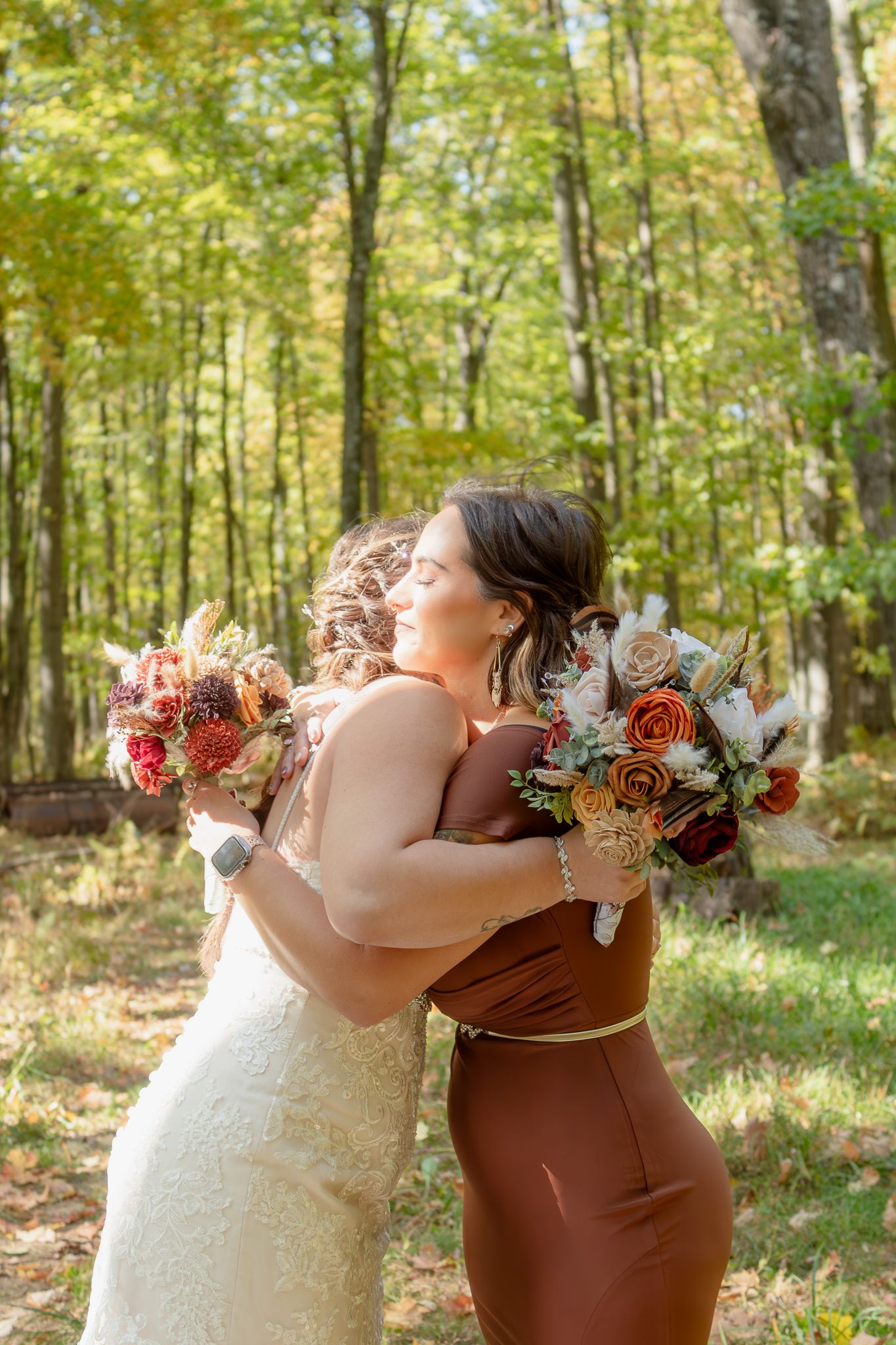 Two people embrace while holding autumn-colored wedding bouquets in a wooded setting.