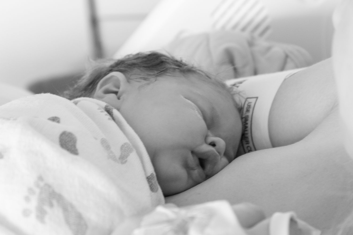 Baby sleeping peacefully on white bedding in black and white photograph.